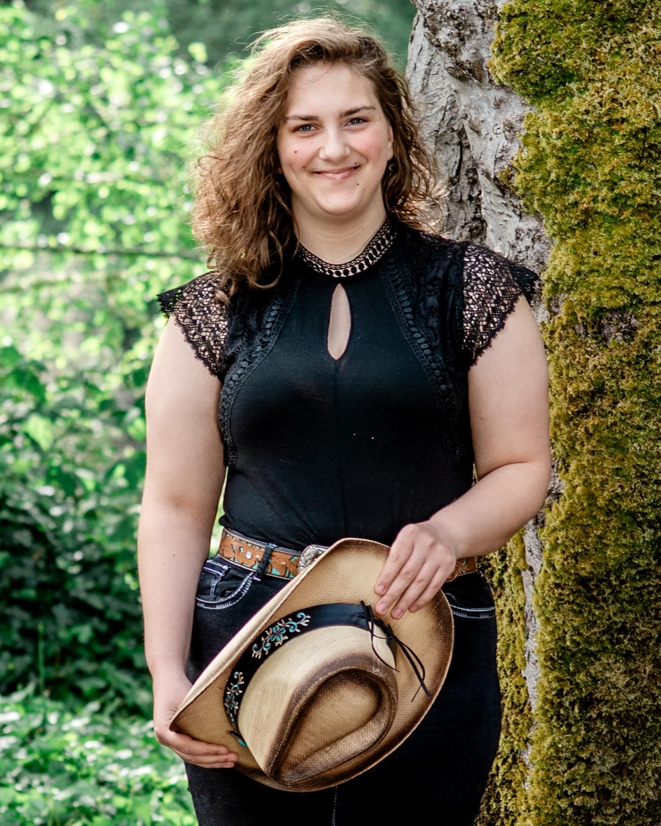 A casual outdoor portrait session featuring someone in black attire leaning against a tree in a lush green setting.