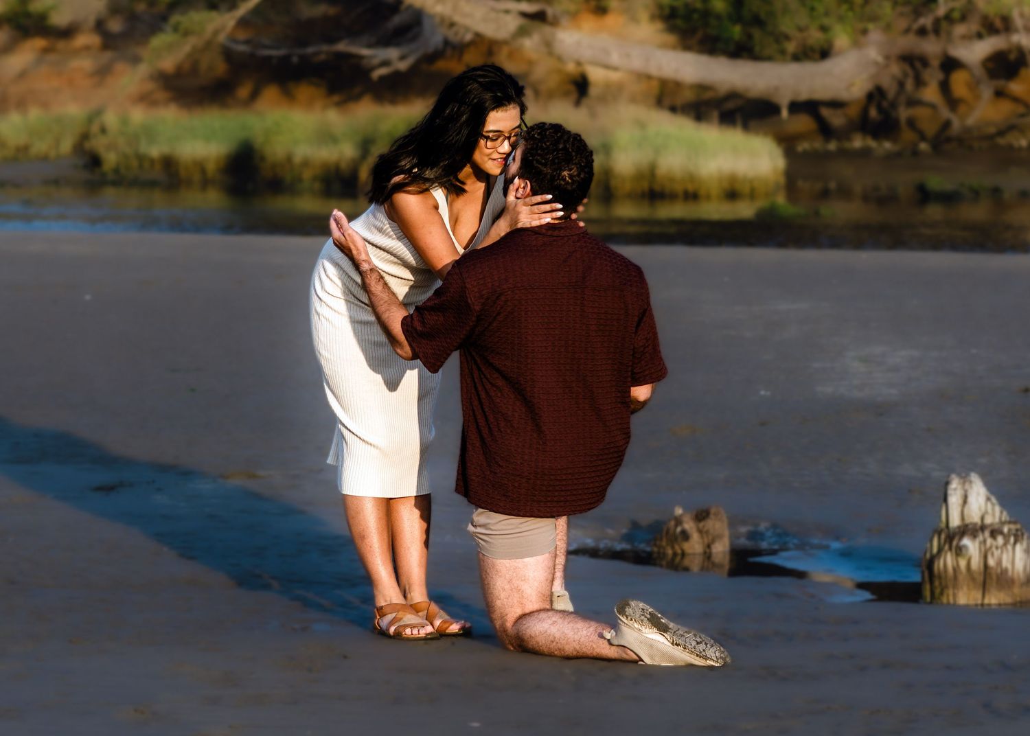Two people share an intimate moment on a rocky beach at sunset.