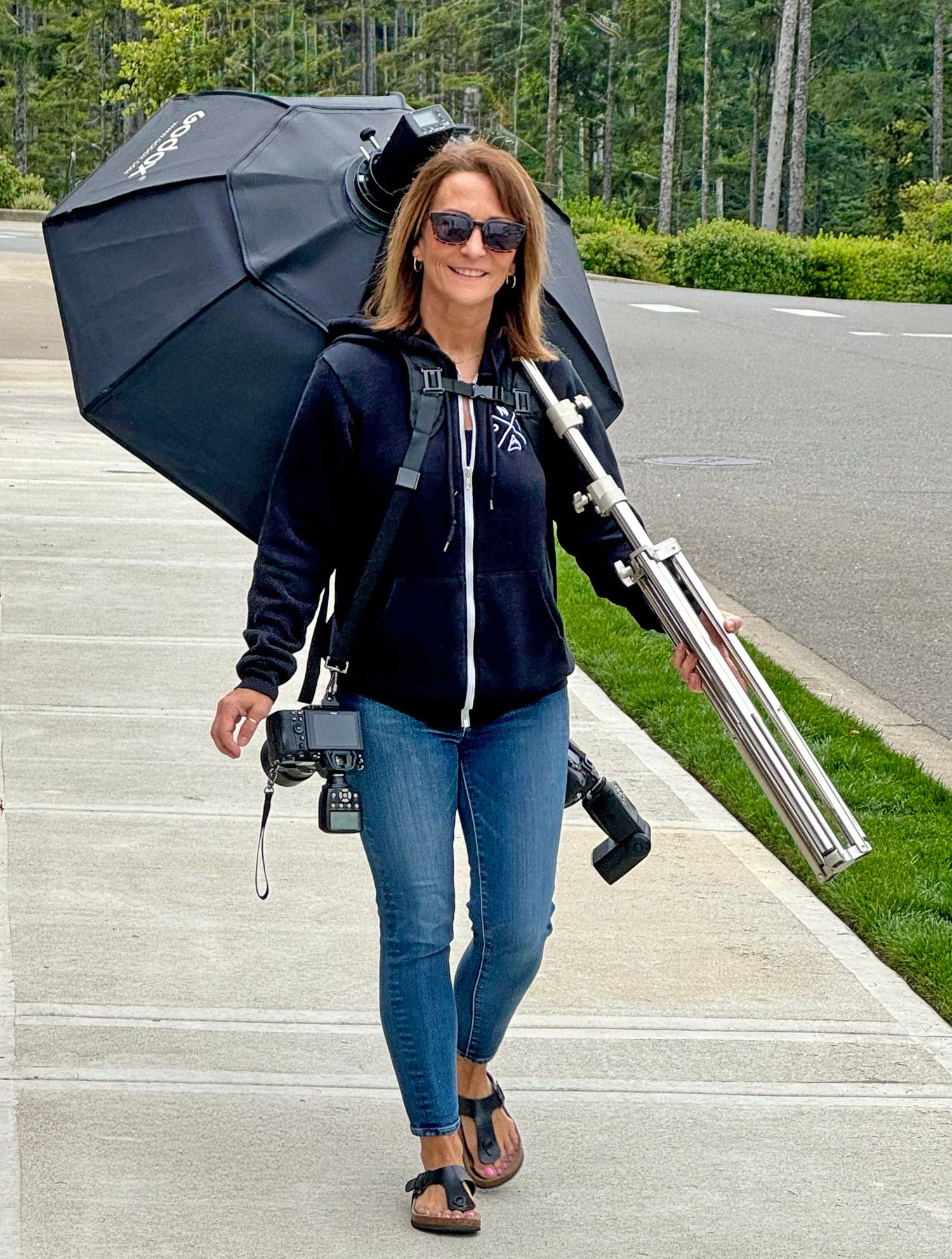 Photographer walking with equipment and black umbrella in a parking lot.