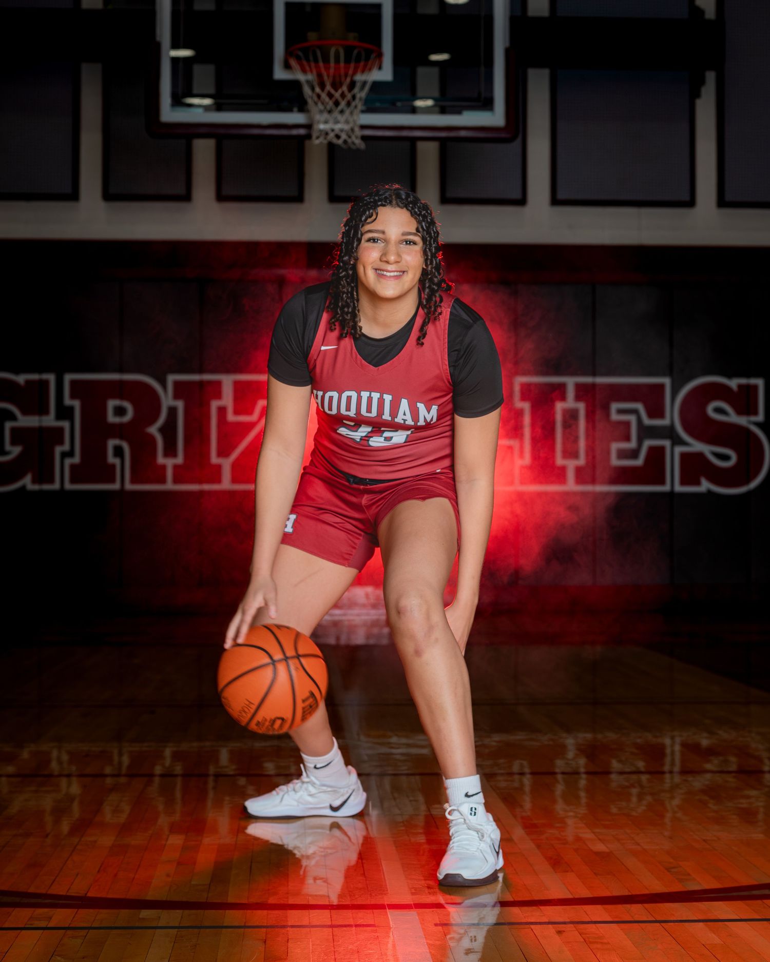 Basketball player in red uniform poses on court with dramatic lighting.
