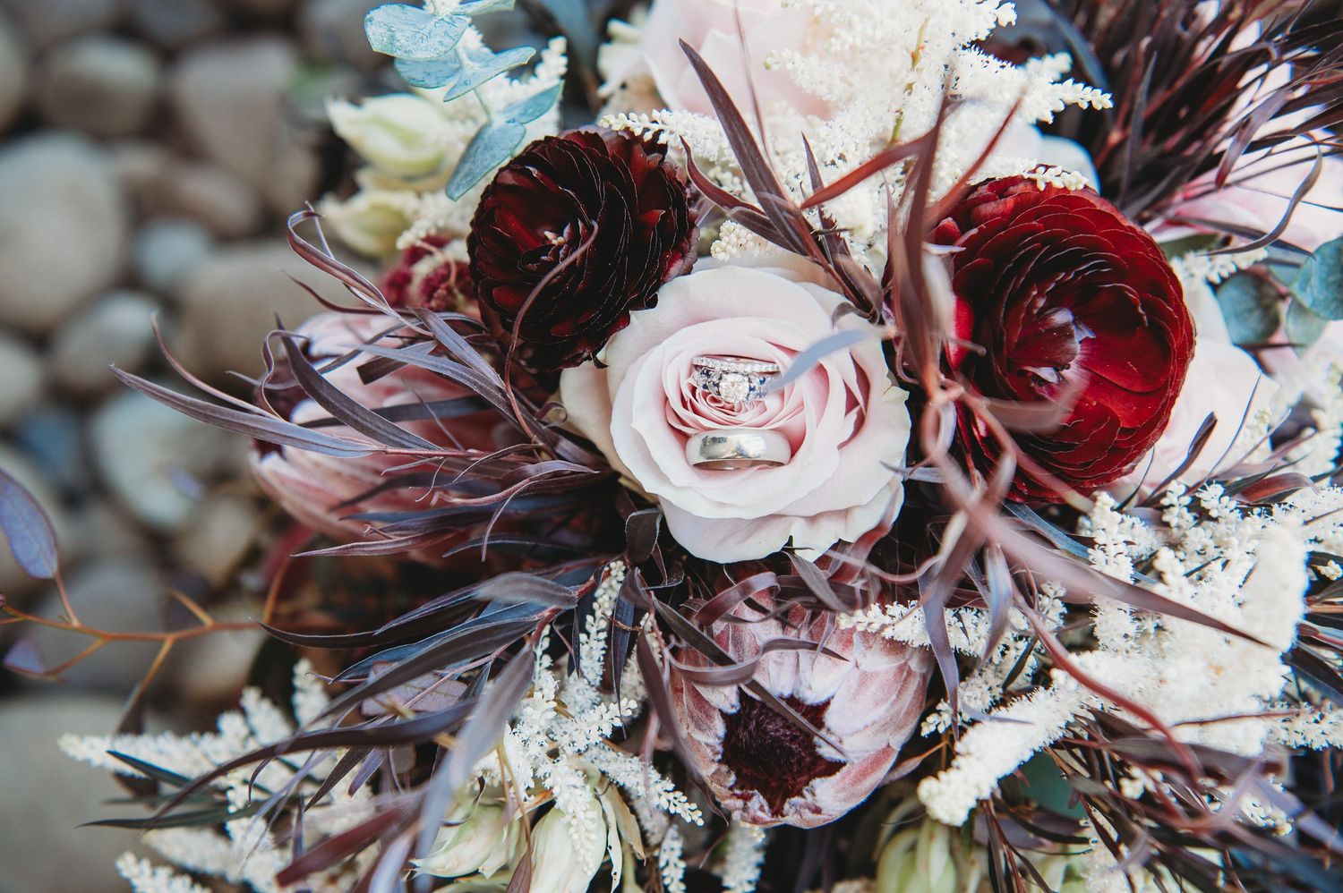 Close-up of a romantic wedding bouquet featuring pink and burgundy roses with wispy textural elements.