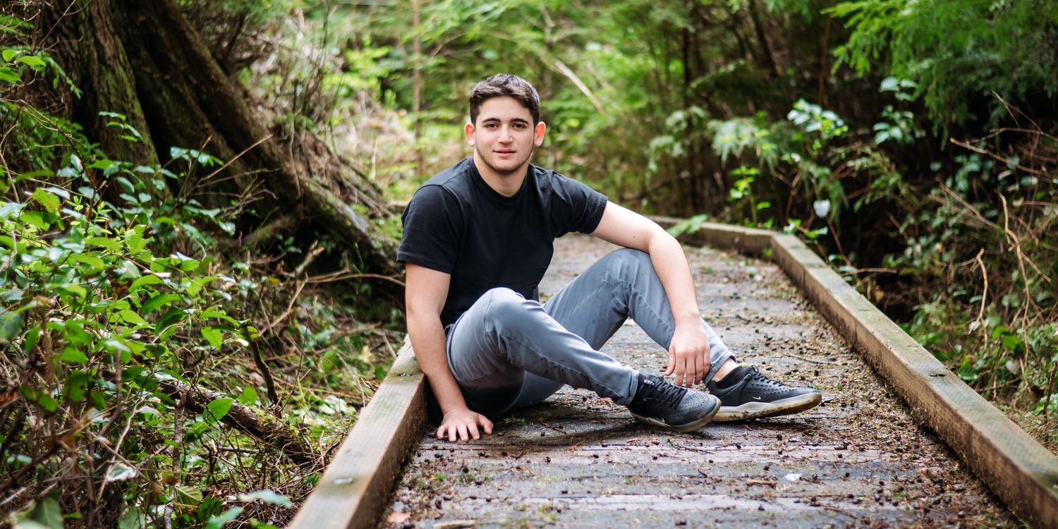 Natural light portrait session on wooden walkway surrounded by lush forest vegetation.