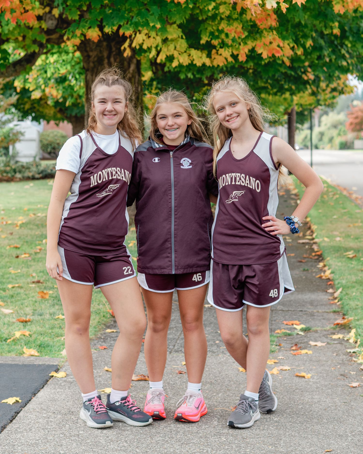Three athletes in maroon uniforms pose together under autumn trees.