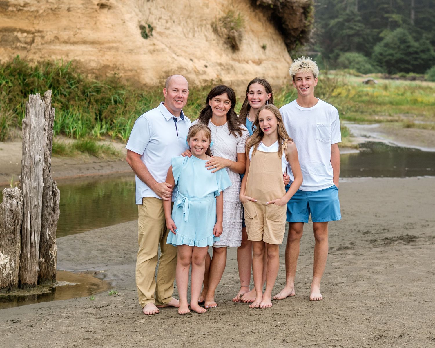 A casual family portrait on a sandy beach with cliffs in the background.