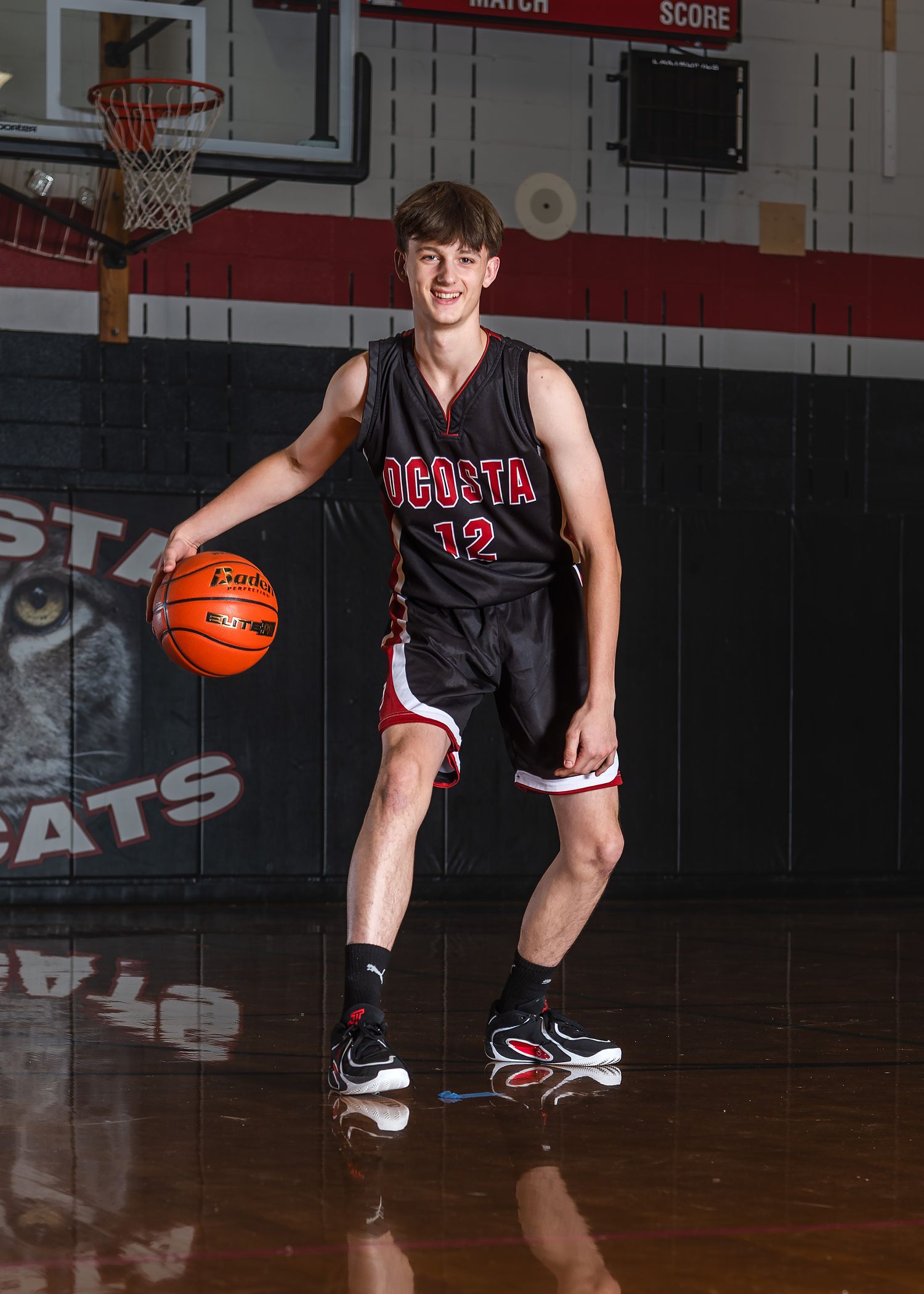 Basketball player in black jersey dribbles ball on indoor court.