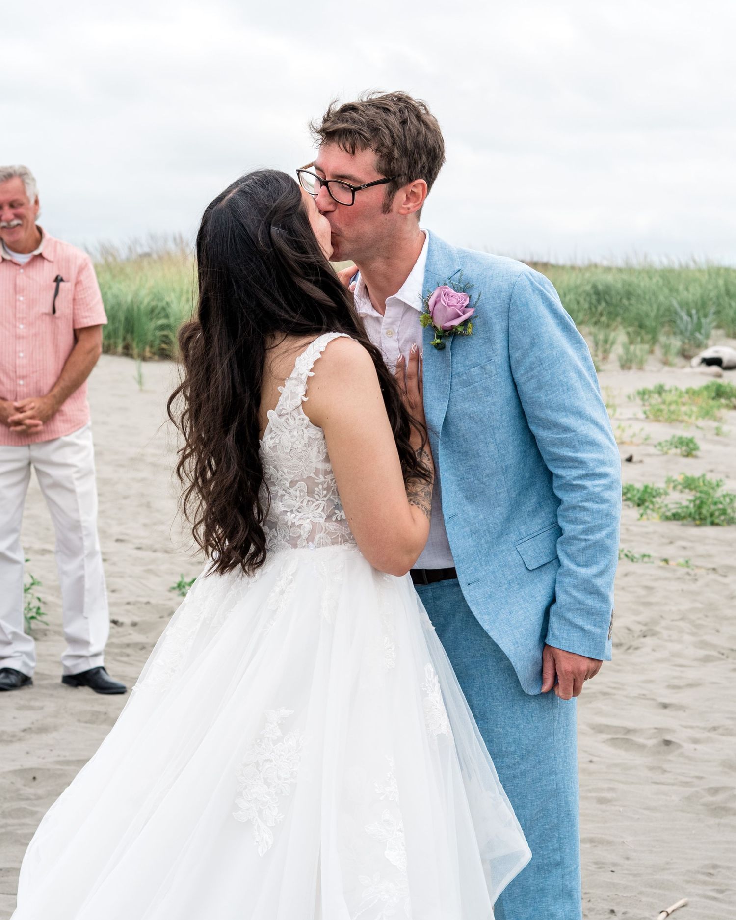 A romantic beach wedding scene with a light blue suit and flowing white dress on the sand.