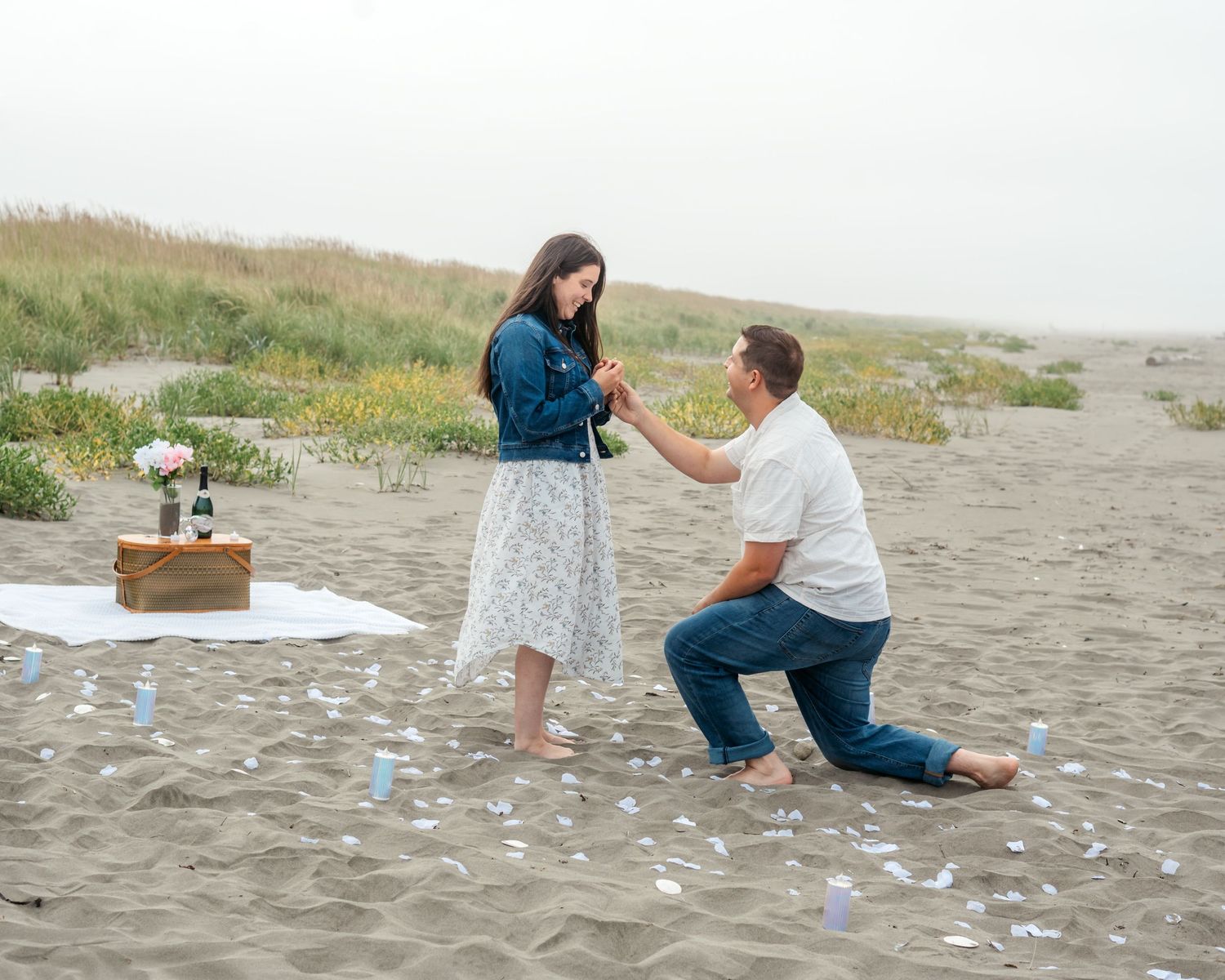 A surprise beach proposal with scattered rose petals on the sand.