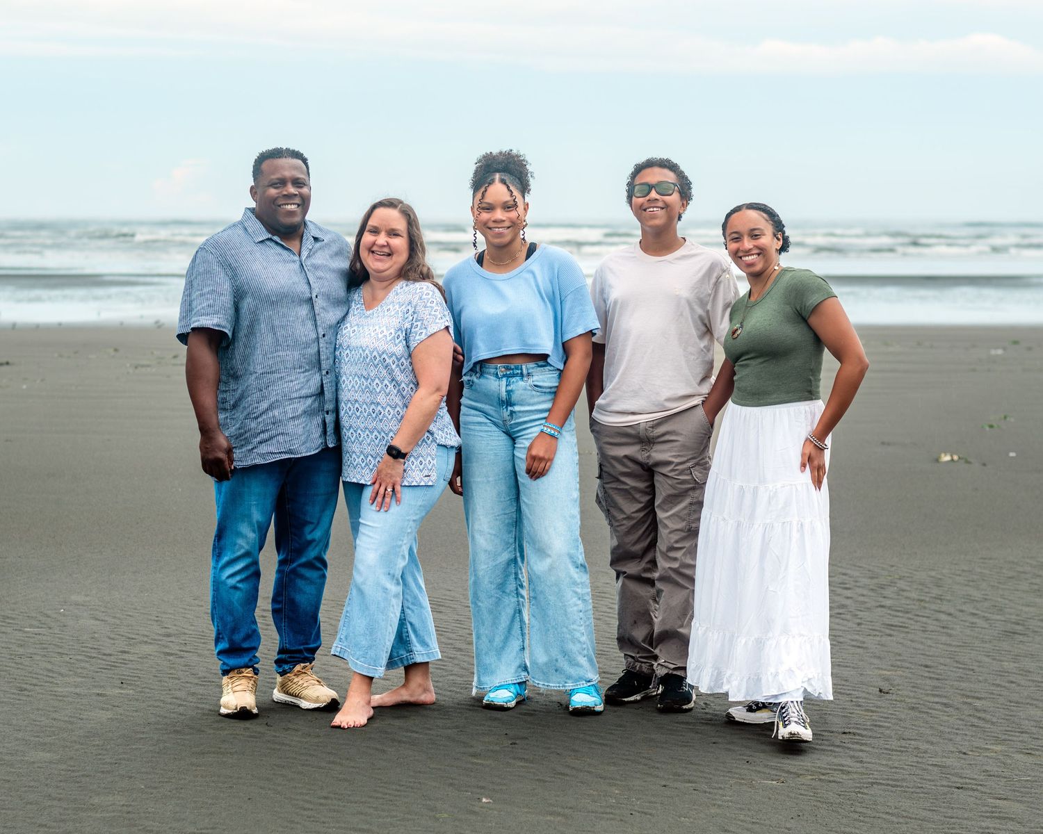 Five people smiling together on a black sand beach with ocean waves in the background.