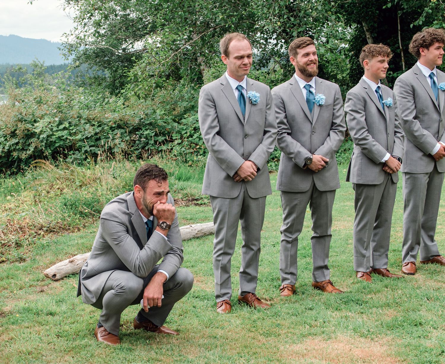 Groomsmen in gray suits pose casually on grassy hillside.