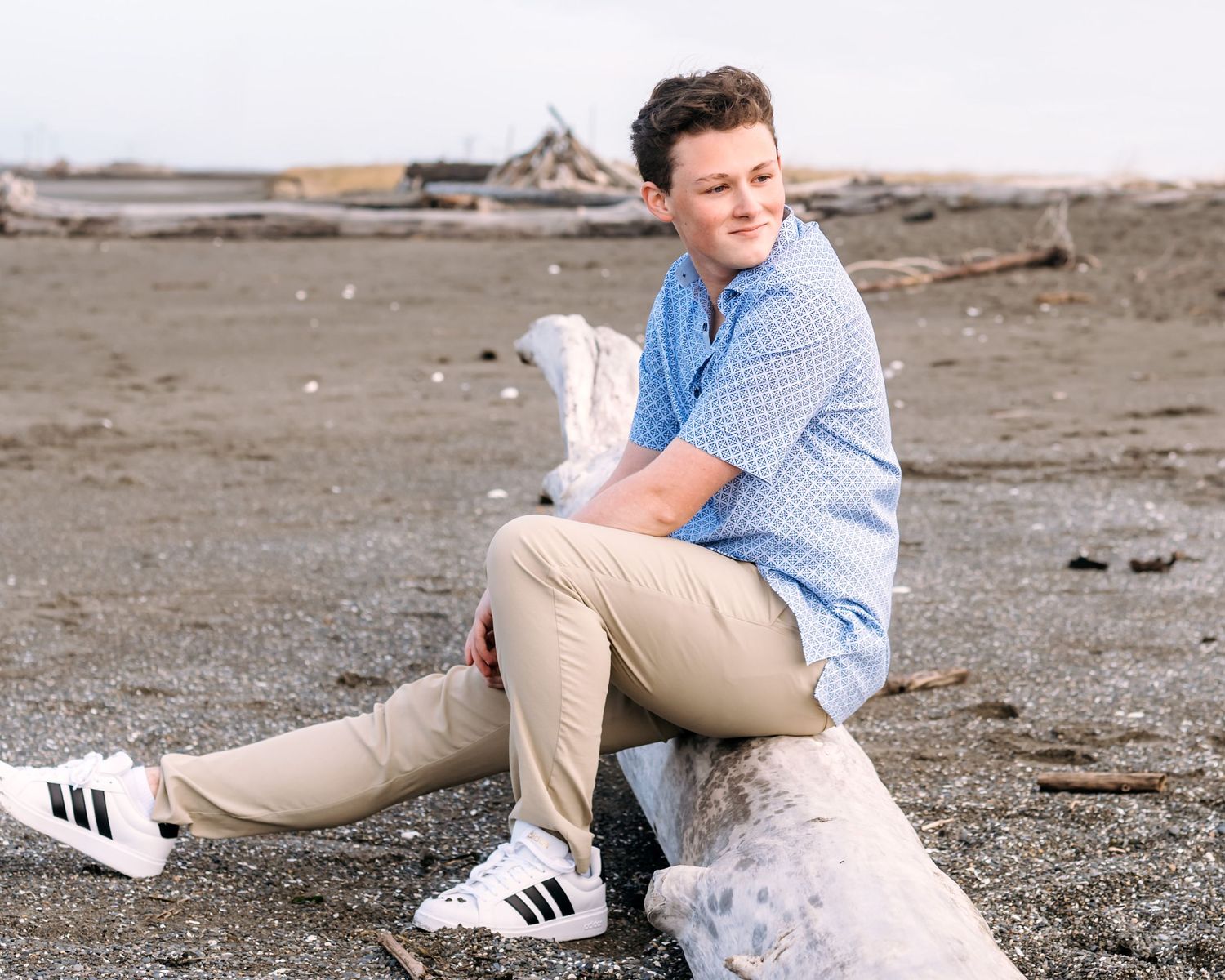 Person in casual attire sitting on rocky ground wearing white sneakers.