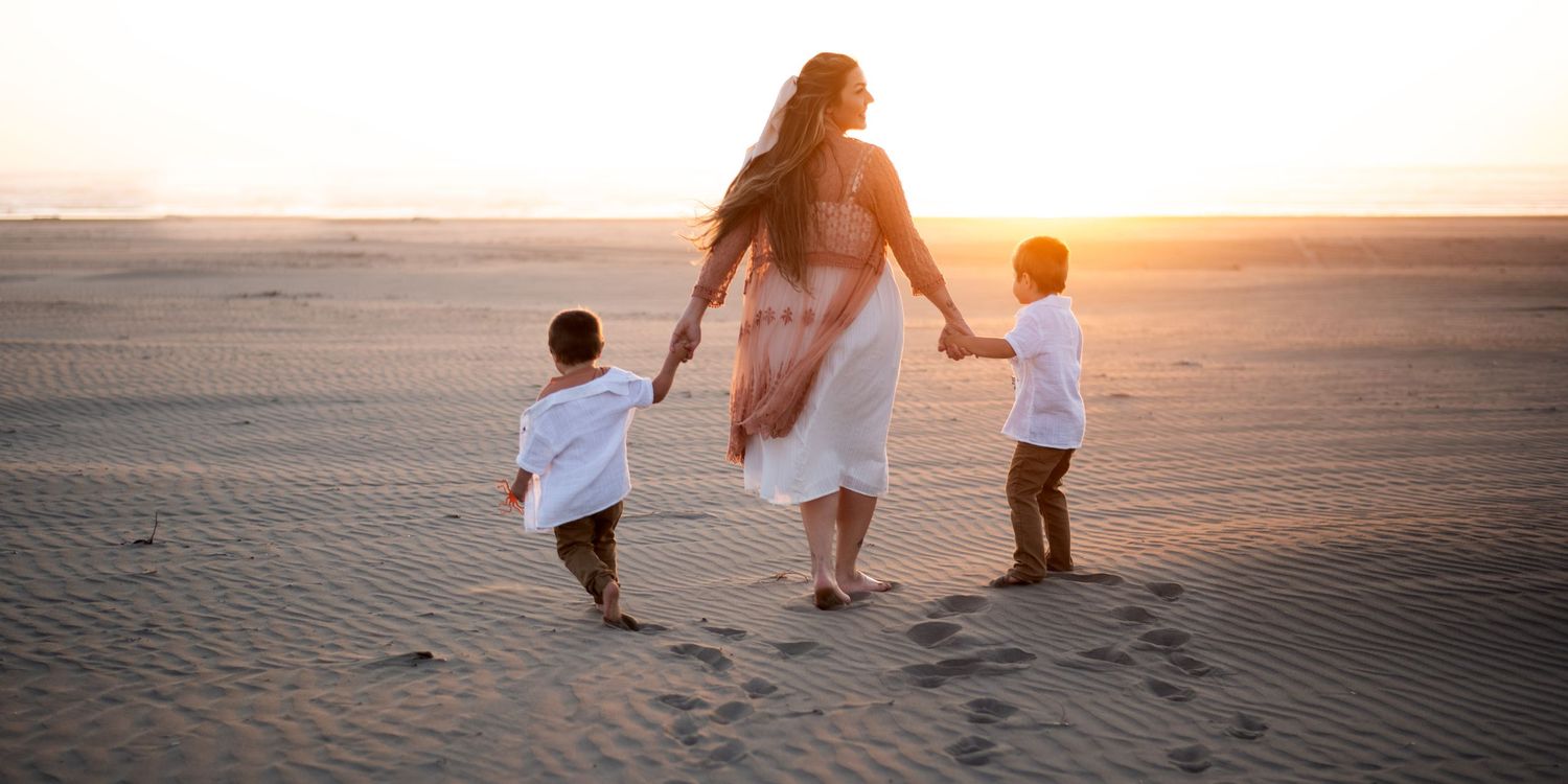 Silhouettes of people walking together on a beach at sunset with golden light reflecting on the sand.