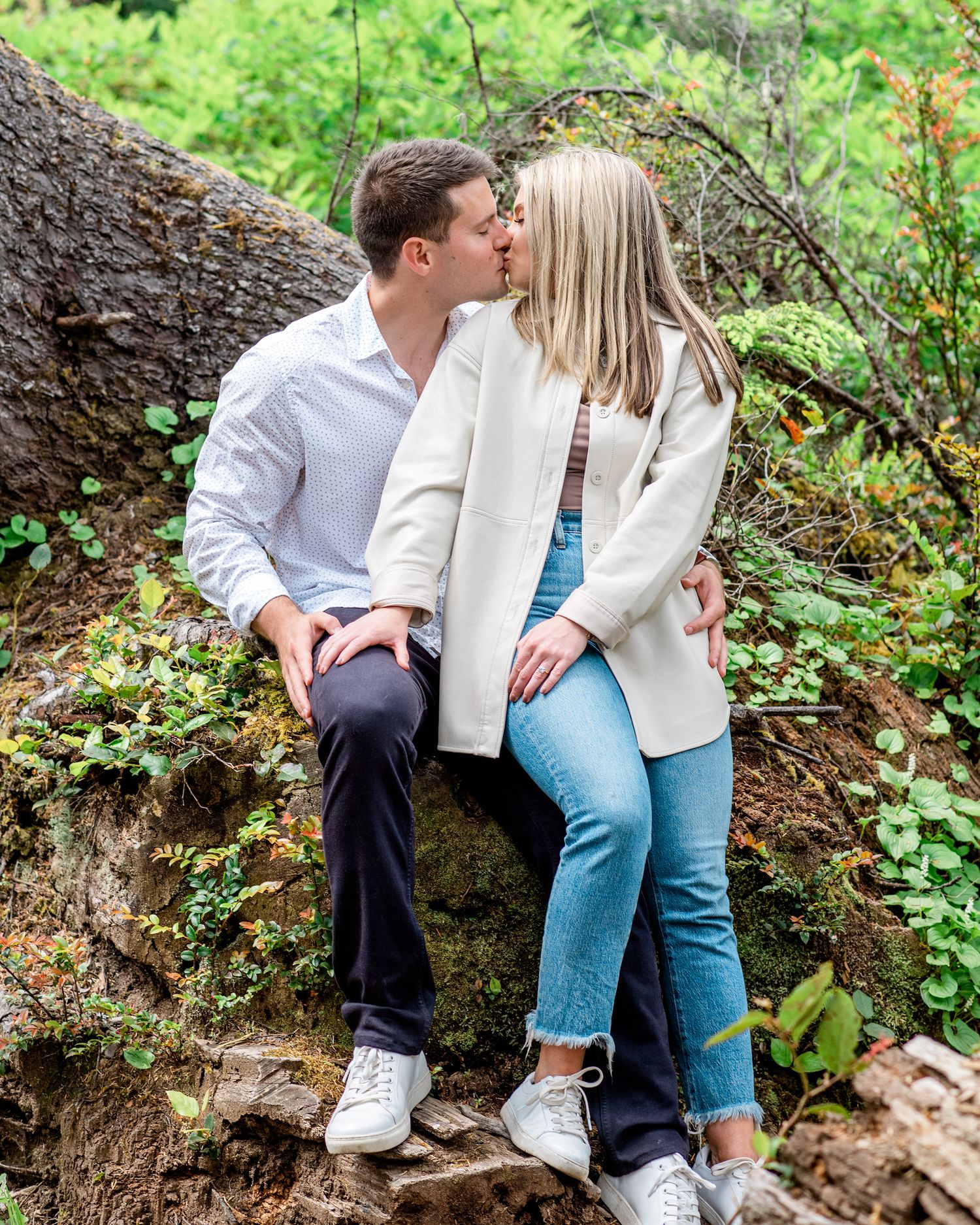 A couple shares intimate moments while sitting on rocks surrounded by lush greenery.