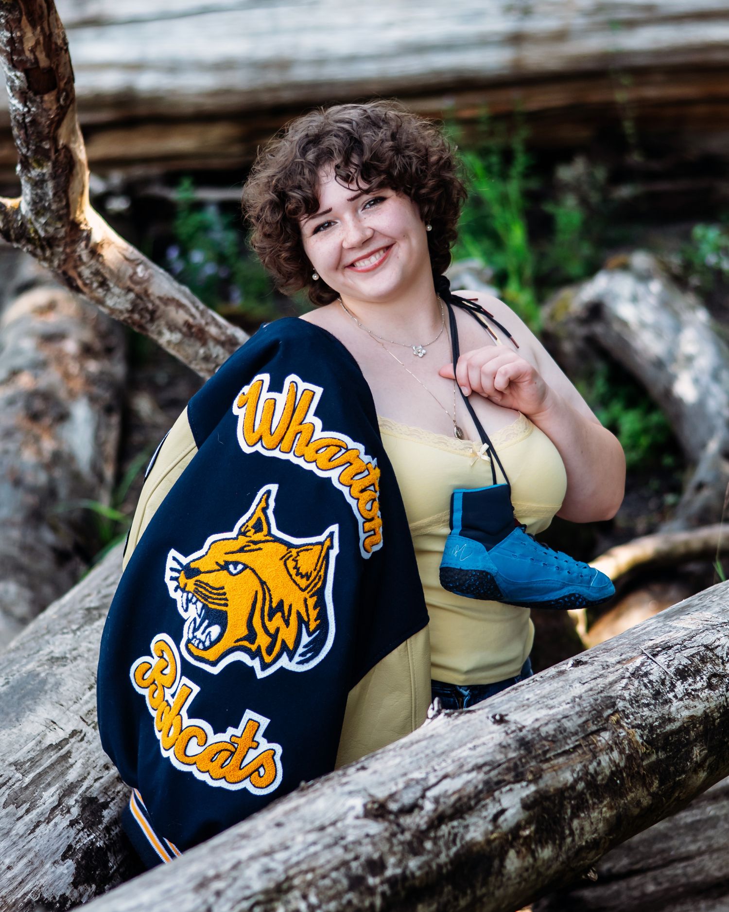 A student poses outdoors with a navy blue varsity jacket featuring a yellow wildcat mascot logo.