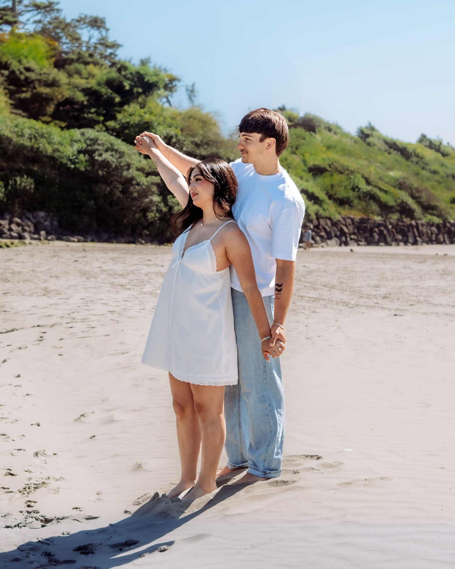 A couple shares a romantic moment while walking along a sunny beach shoreline.