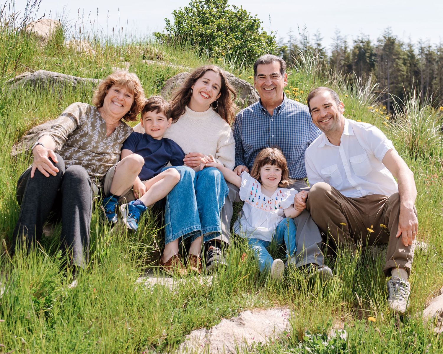 Happy family of six smiling together on a grassy hillside on a sunny day outdoors.