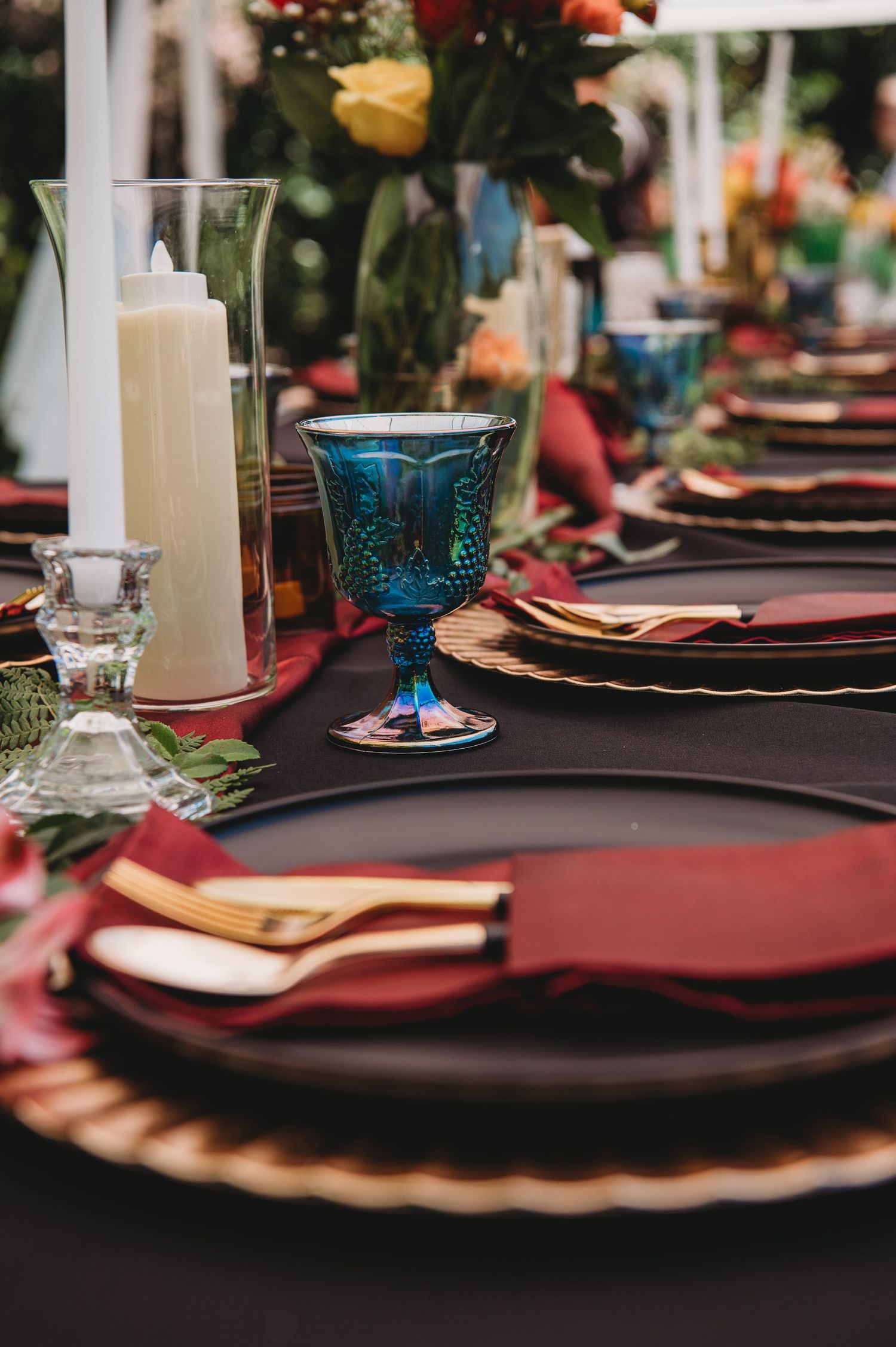 Elegant table setting with burgundy napkins, gold chargers, and blue goblets for a formal dinner.