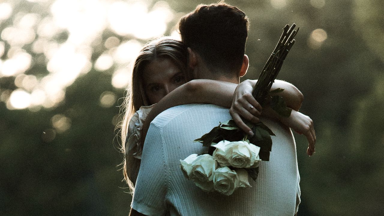 Couple embracing in golden sunlight with white roses in hand.