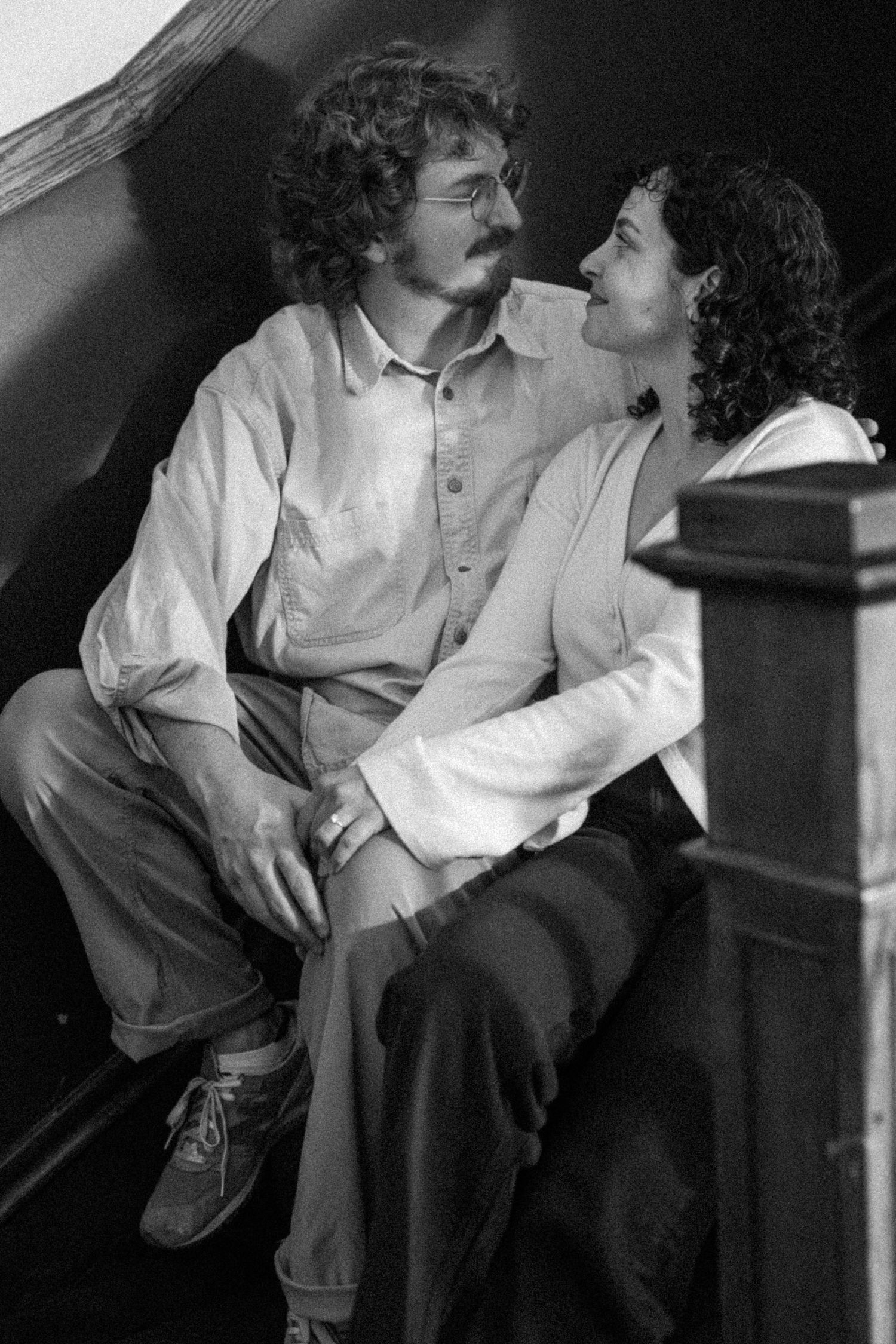 Black and white photo of a couple sitting on stairs, gazing at each other affectionately in a romantic moment.