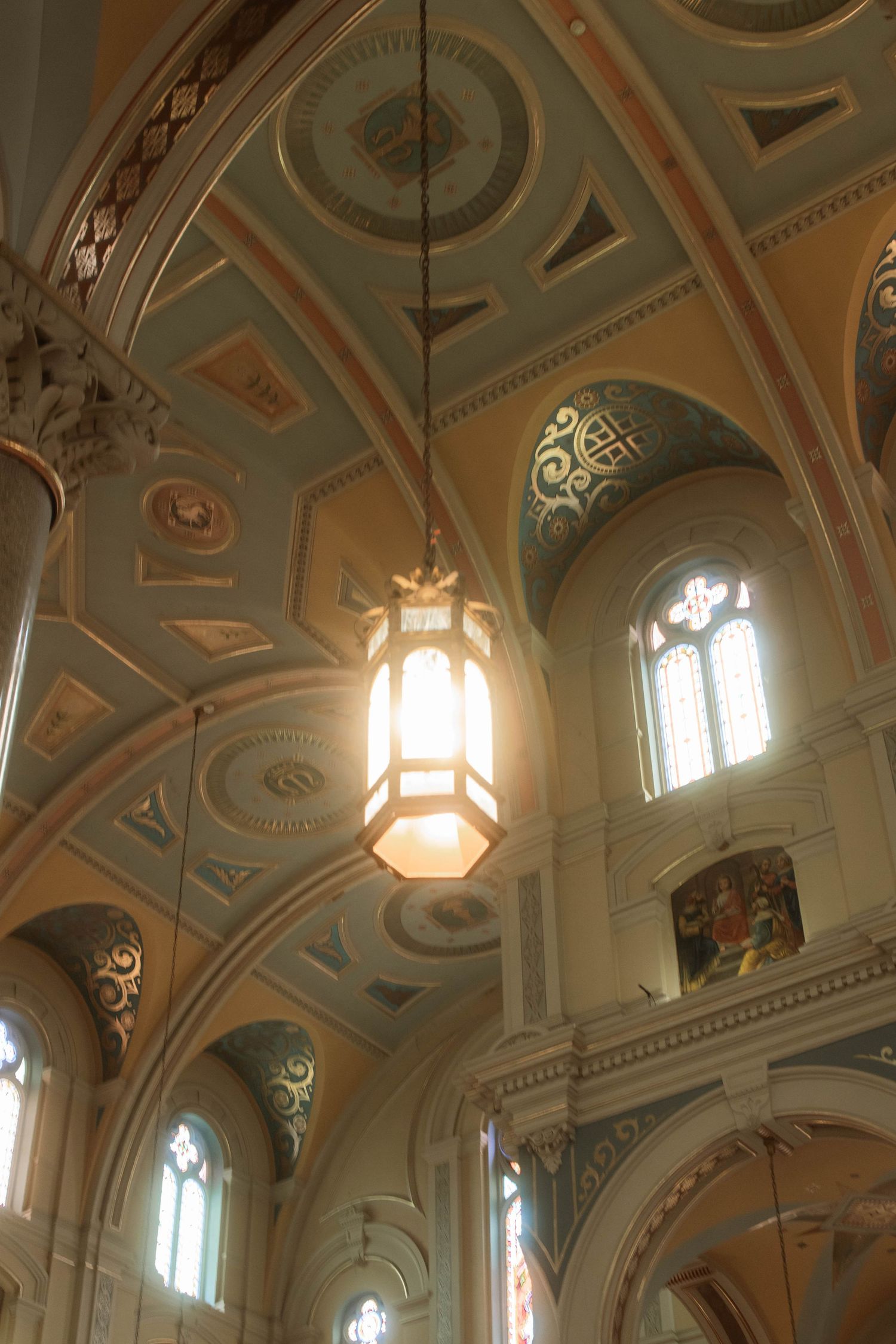 Ornate cathedral interior featuring decorative vaulted ceilings, glowing lantern, stained glass windows, and colorful painted arches.