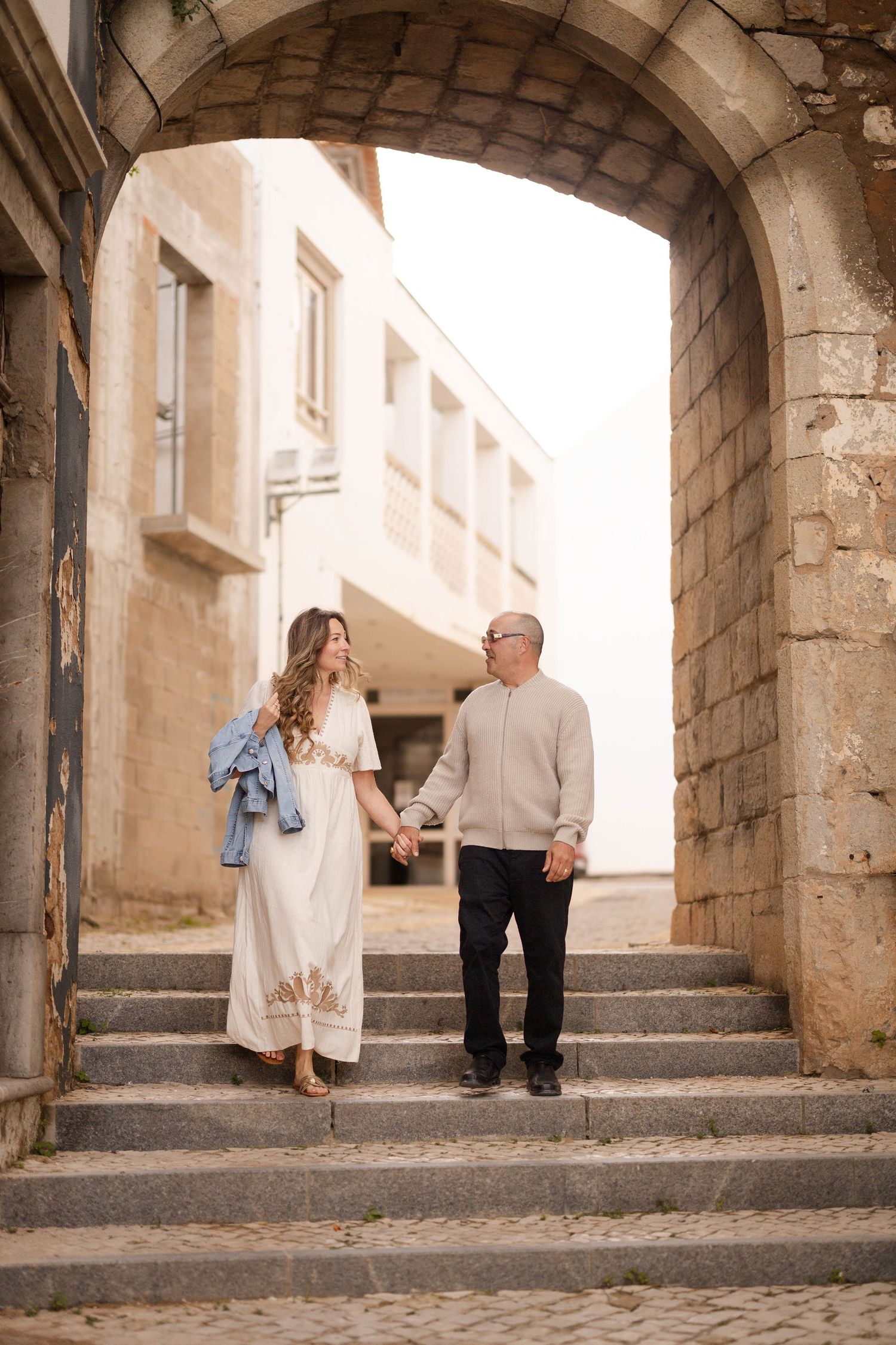 Couple holding hands walking down stone steps under an arch in a charming European old town street.