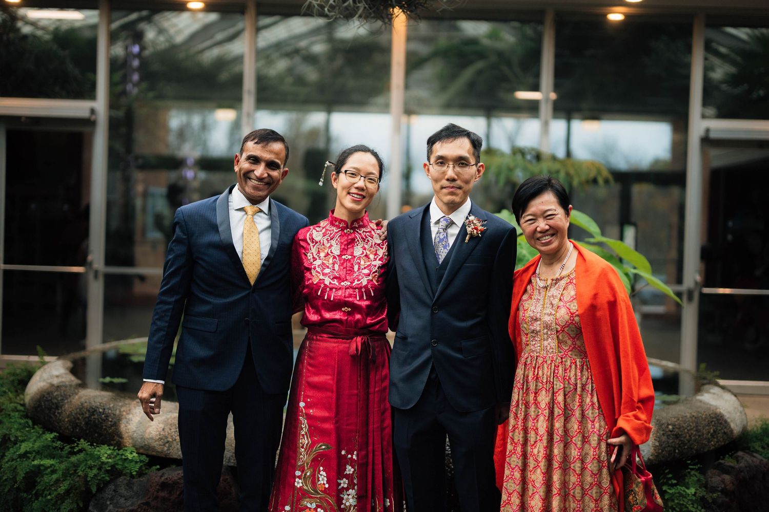 A group celebrates at an outdoor event wearing formal attire including red and orange traditional dresses.