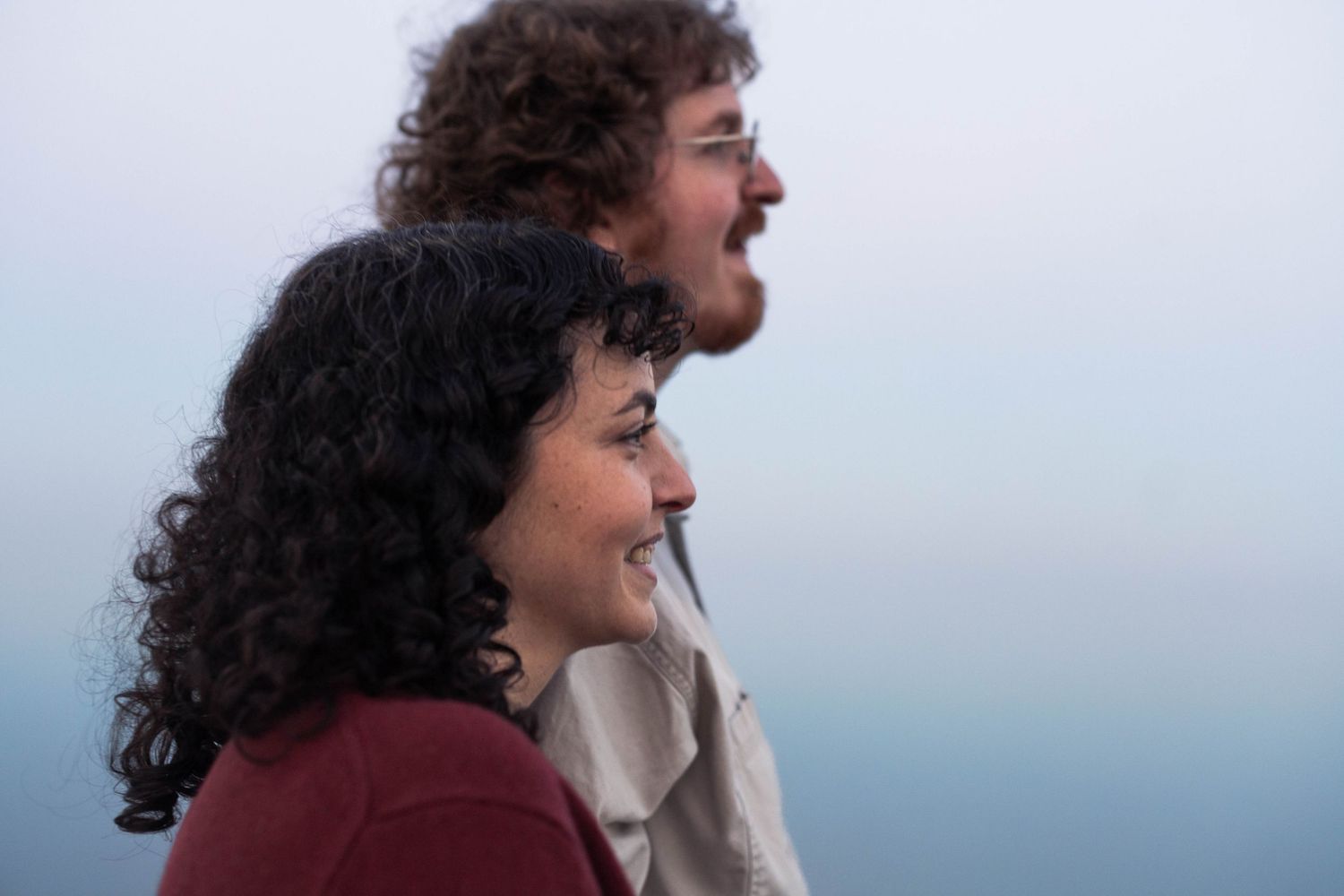 Smiling couple with curly hair standing side by side against misty background outdoors.