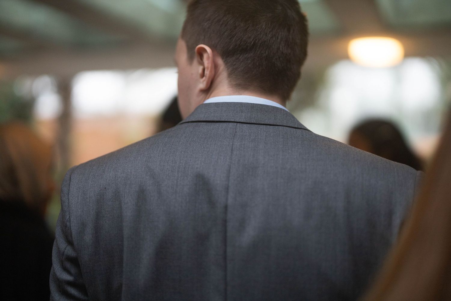 Back view of a man in a gray suit at a formal event or wedding reception.