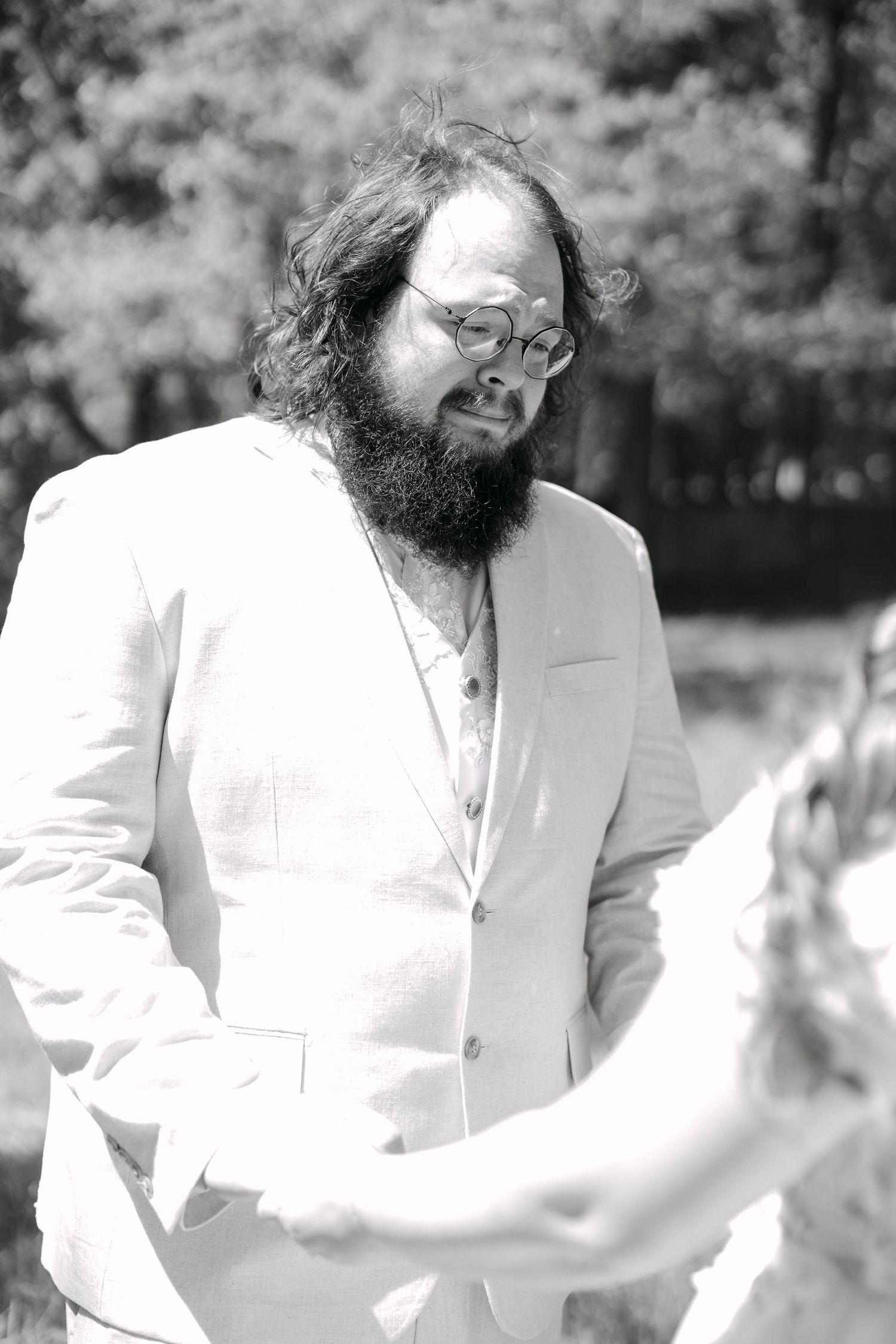Bearded man with glasses in white suit outdoors, black and white portrait photo.