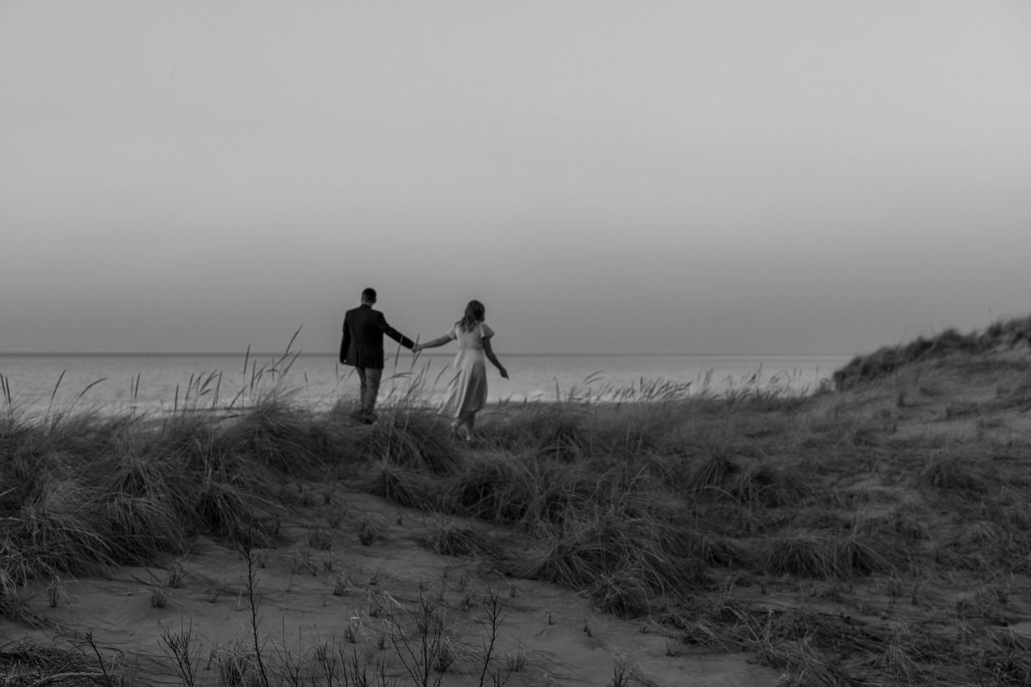 Black and white silhouettes of people walking on a hillside against a moody sky.