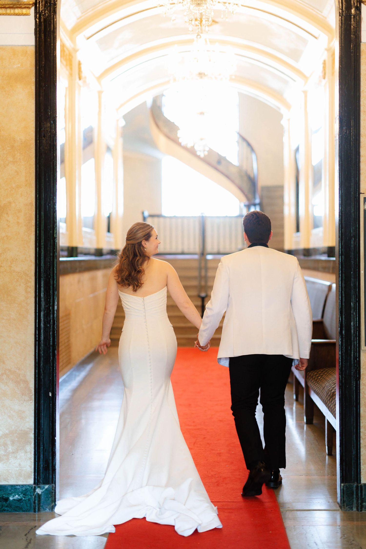 Bride and groom walk hand in hand down red carpet aisle.