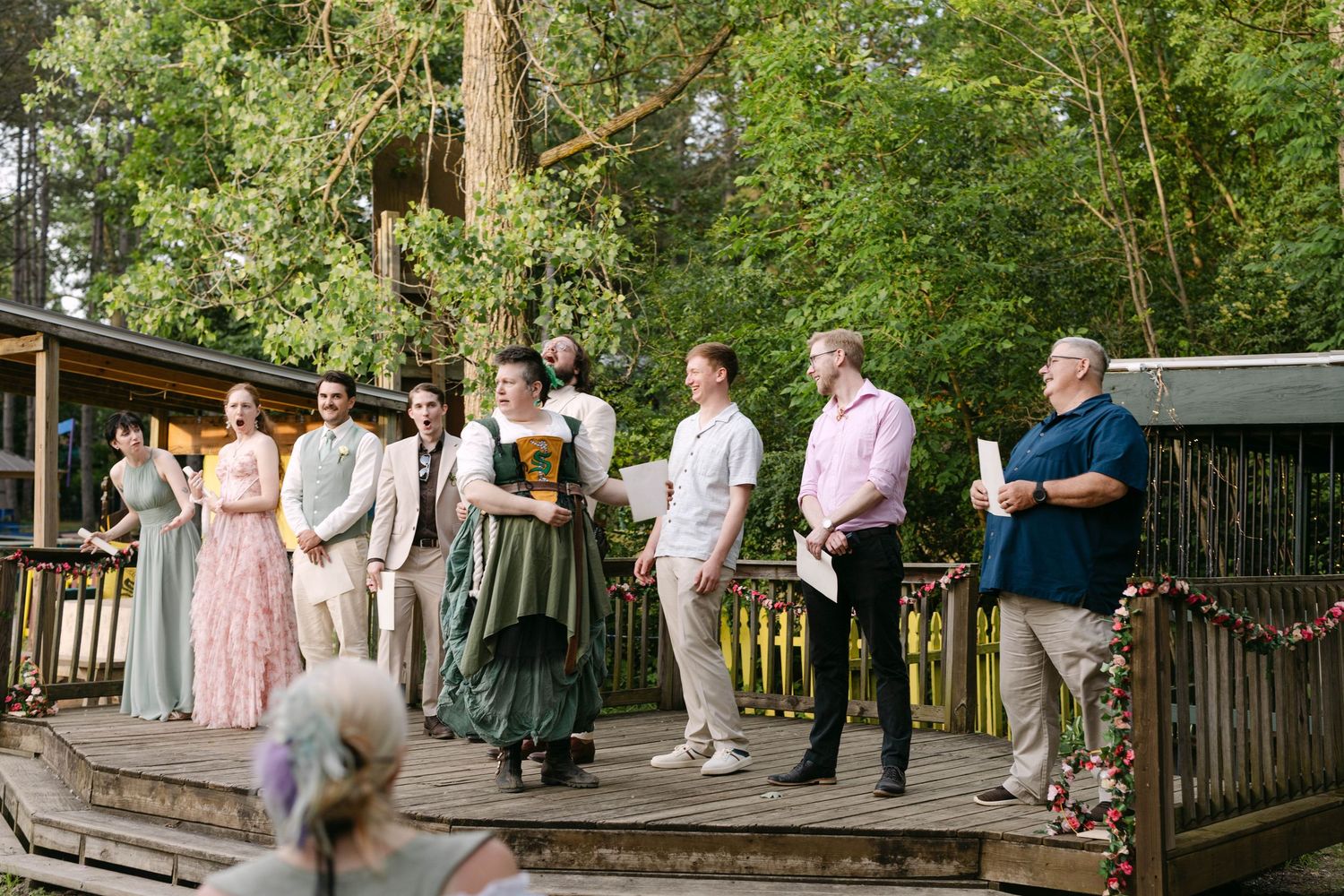 Wedding party stands on a wooden deck surrounded by trees during an outdoor forest ceremony.