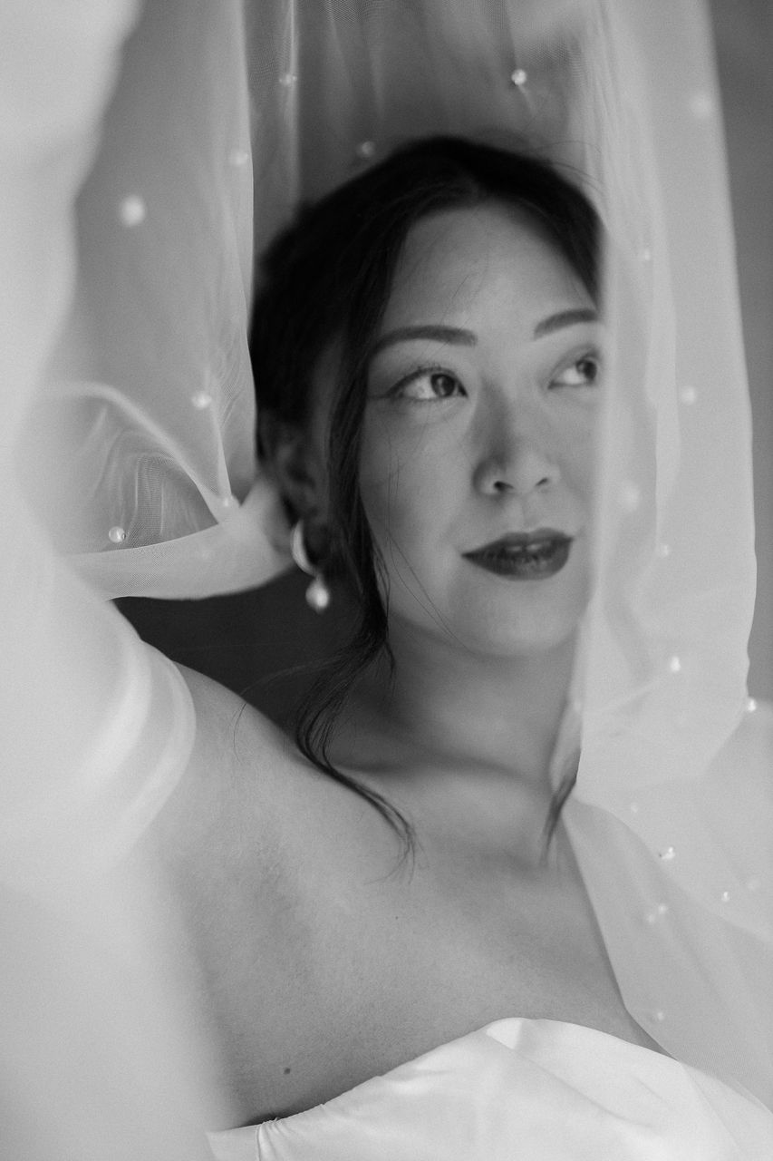 Artistic bridal portrait through sheer white veil with soft lighting effects.