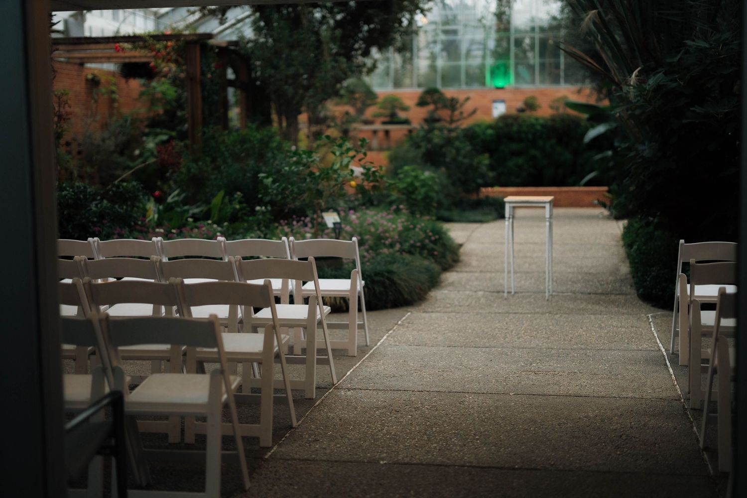 Elegant outdoor wedding ceremony setup with white folding chairs along a garden pathway surrounded by lush greenery.