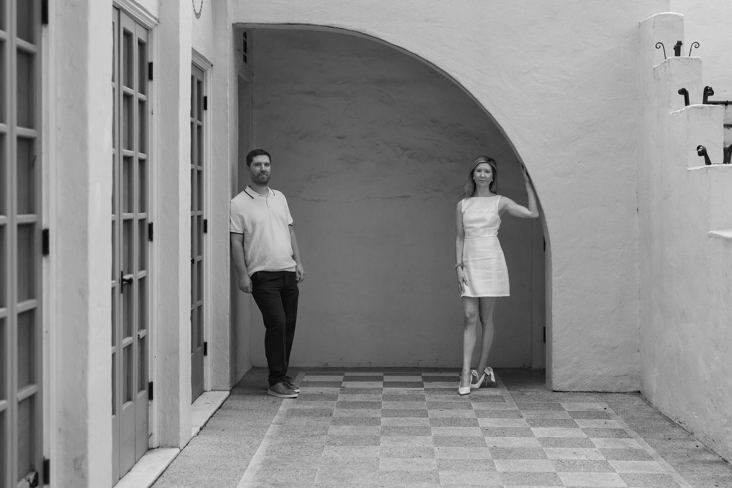 Black and white photo of a man and woman standing apart under an arched doorway in a courtyard.
