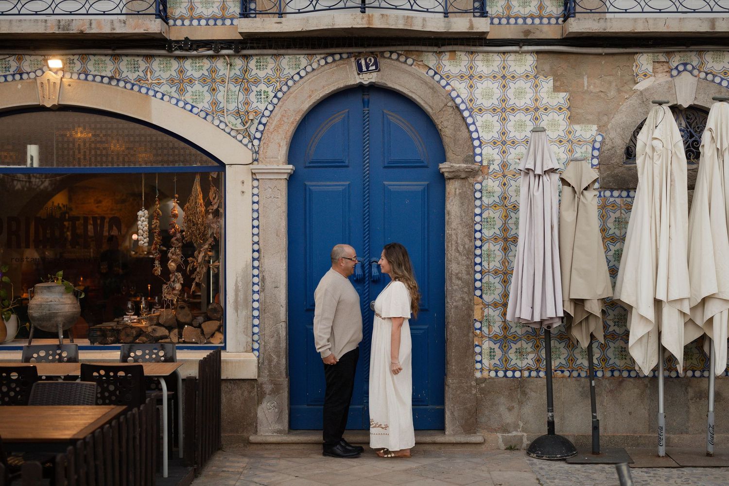 Couple standing before a blue door on a tiled facade in Porto, Portugal, sharing a romantic moment.
