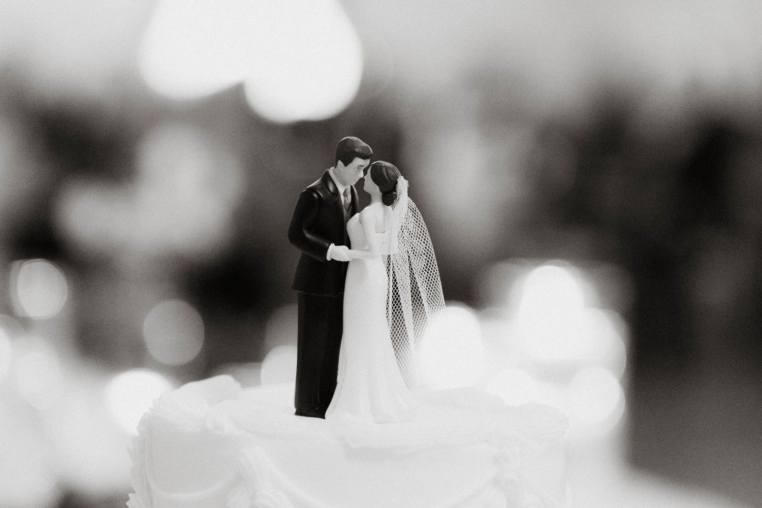 Black and white photo of a bride and groom wedding cake topper figurine kissing on a white cake.