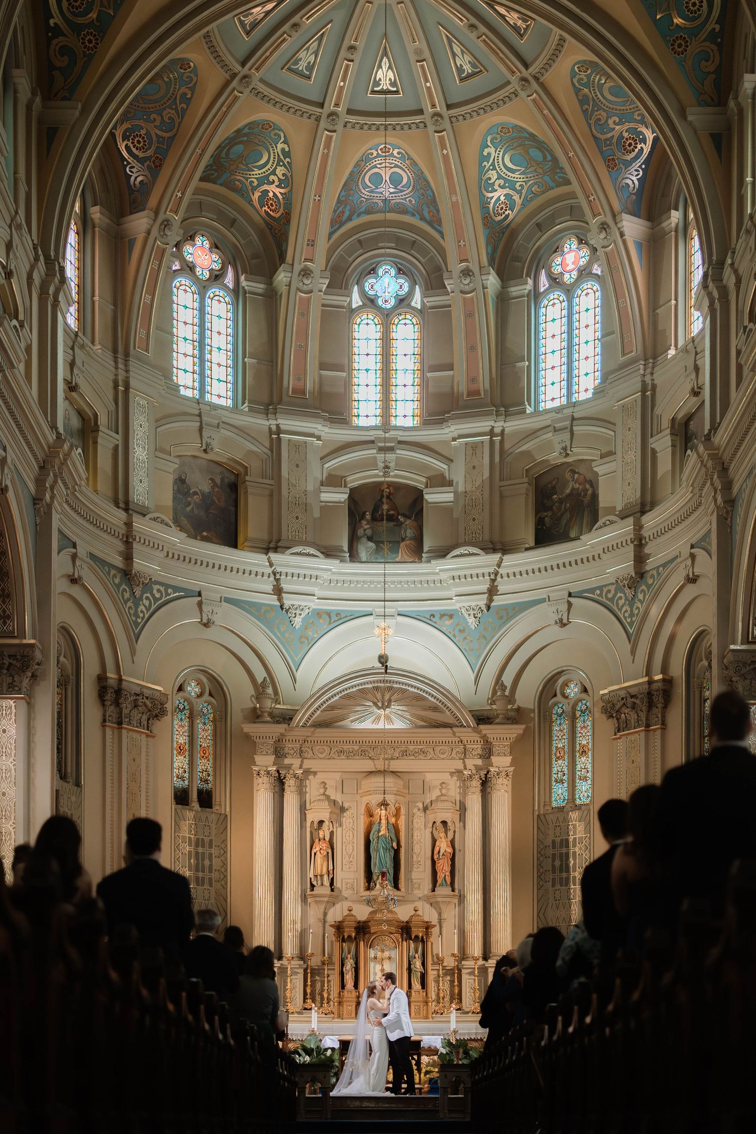 Couple exchanges vows at ornate church altar beneath stunning domed ceiling with stained glass windows.