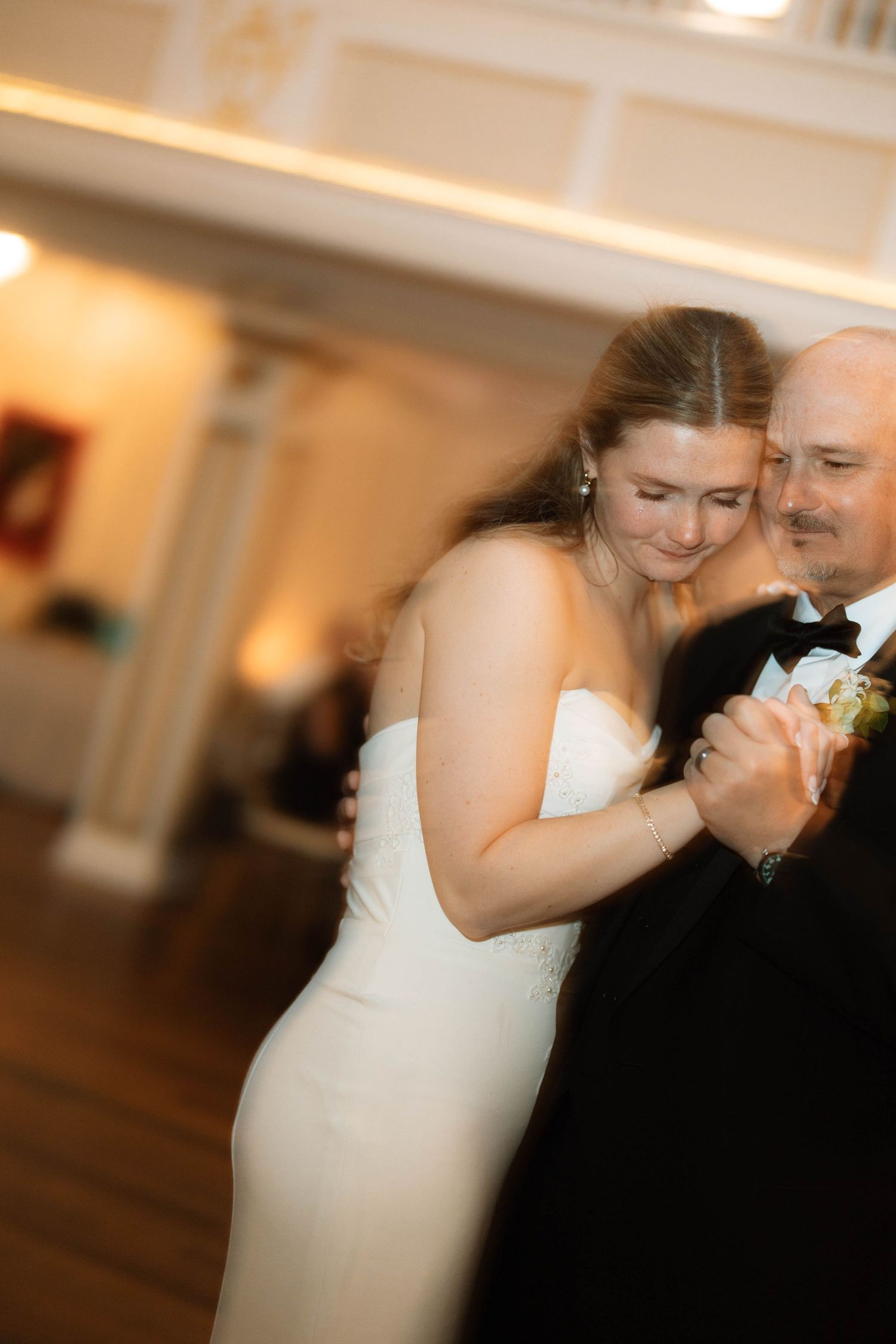 Bride in white strapless gown shares an intimate father-daughter dance at elegant indoor wedding reception.