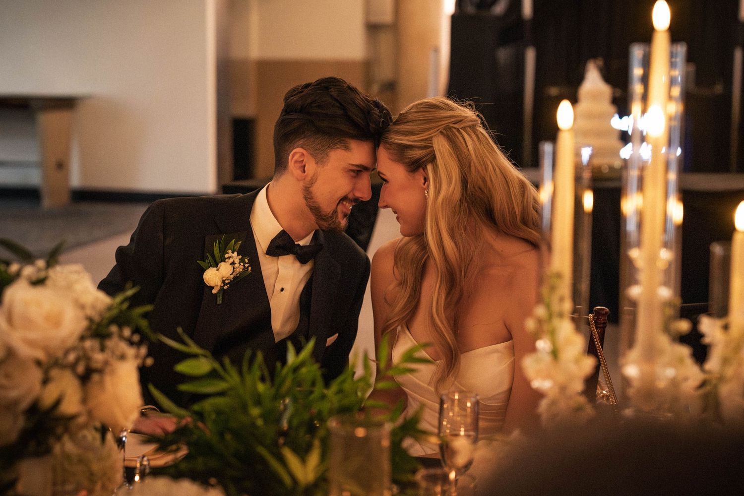 Bride and groom share an intimate moment at their candlelit wedding reception sweetheart table.