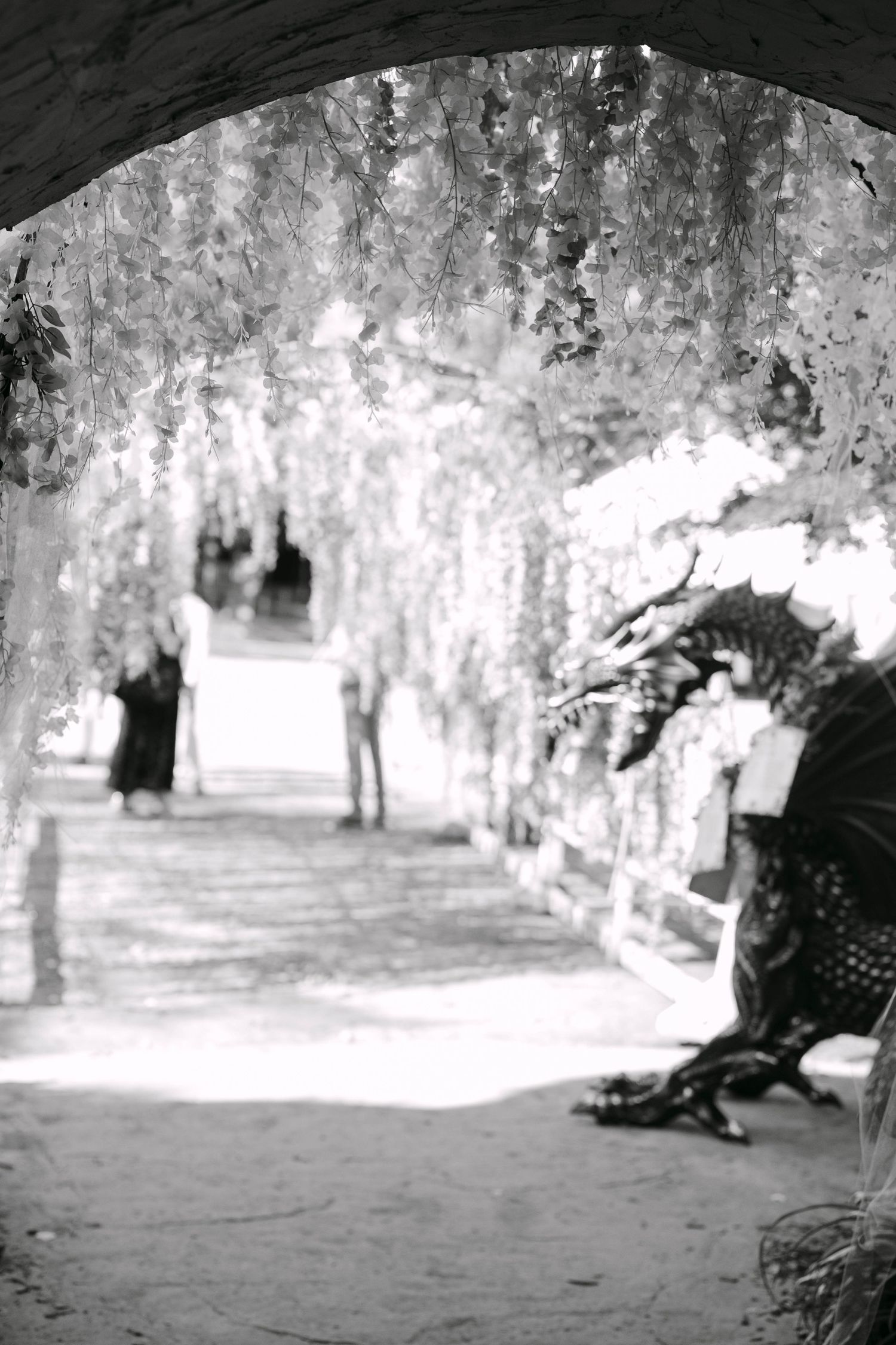 Black and white photo of a floral-draped garden tunnel walkway at an elegant outdoor wedding venue.