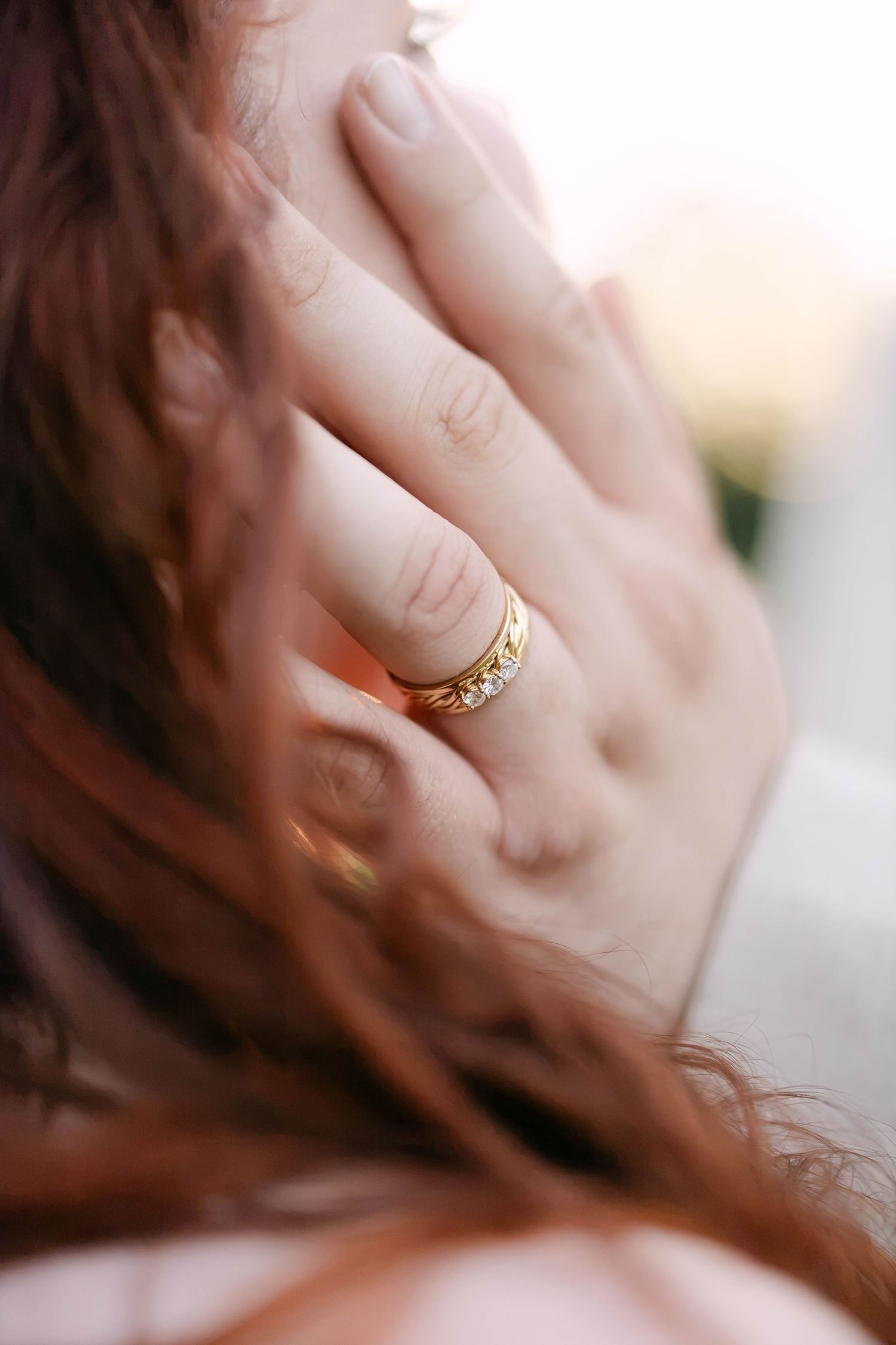Close-up of a gold diamond ring on a woman's finger with red hair in the background.