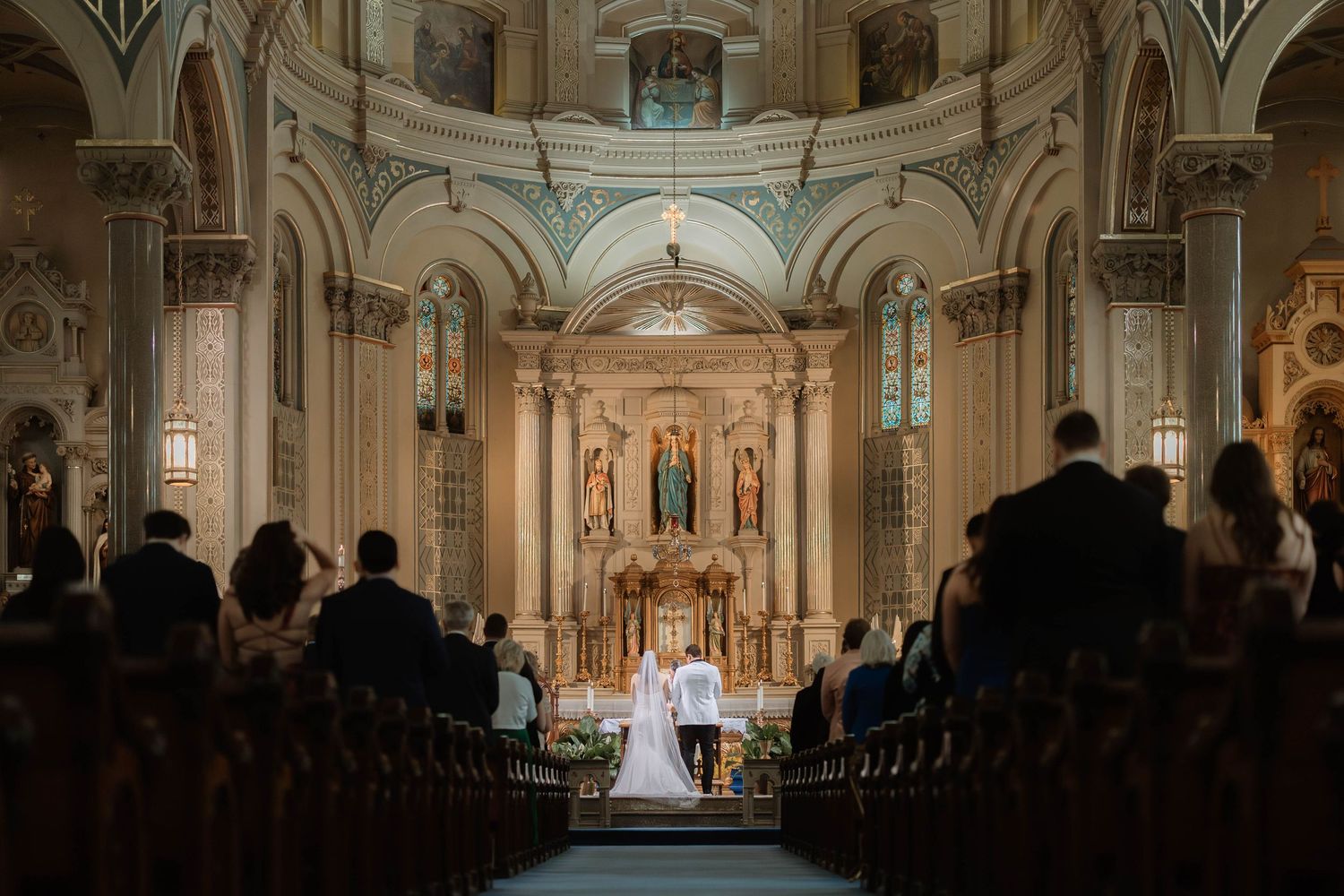 Elegant church wedding ceremony at ornate altar with bride and groom surrounded by guests in grand cathedral.