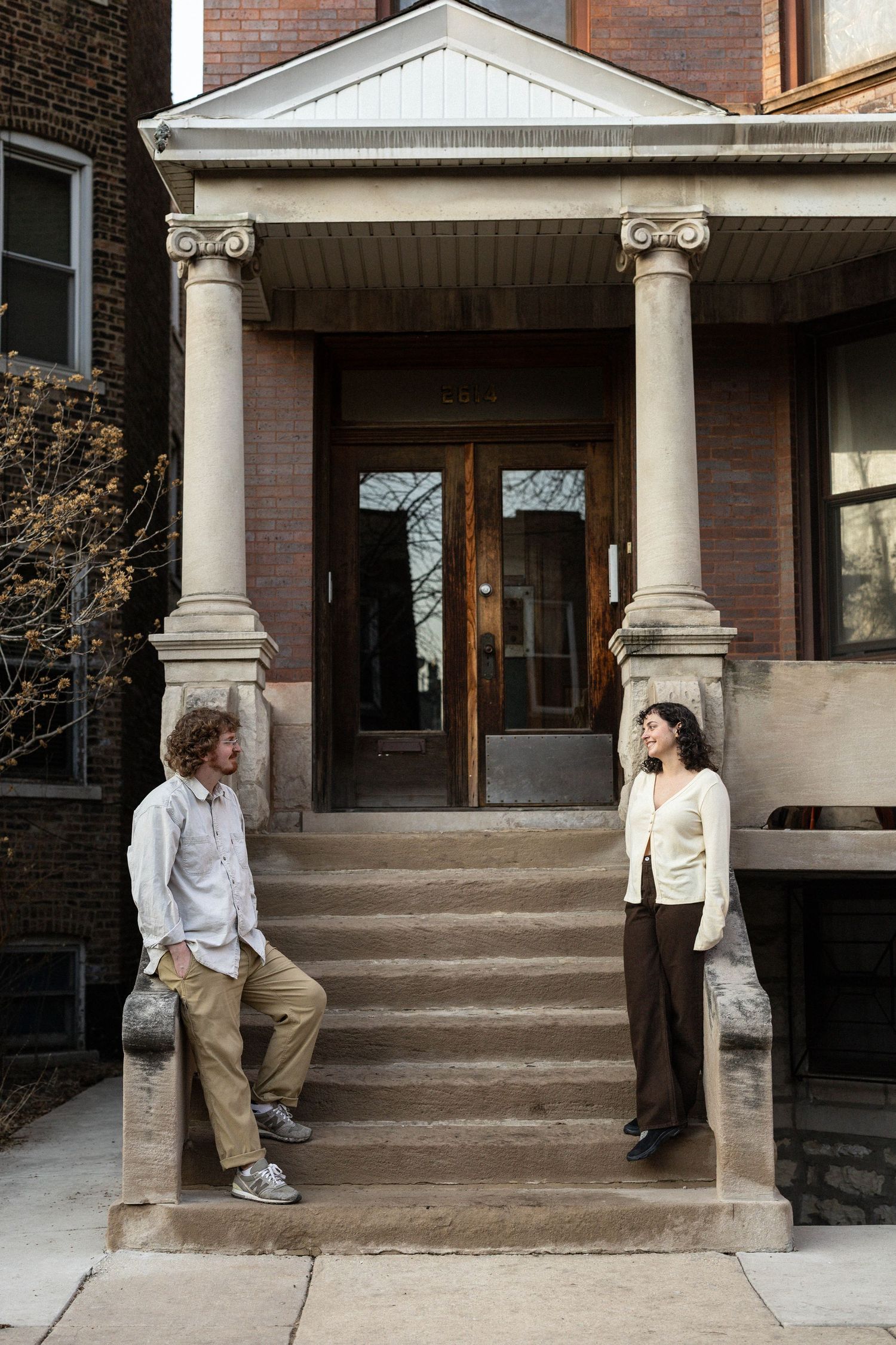 A man and woman stand on opposite sides of stone steps outside a classic brick building with tall columns.