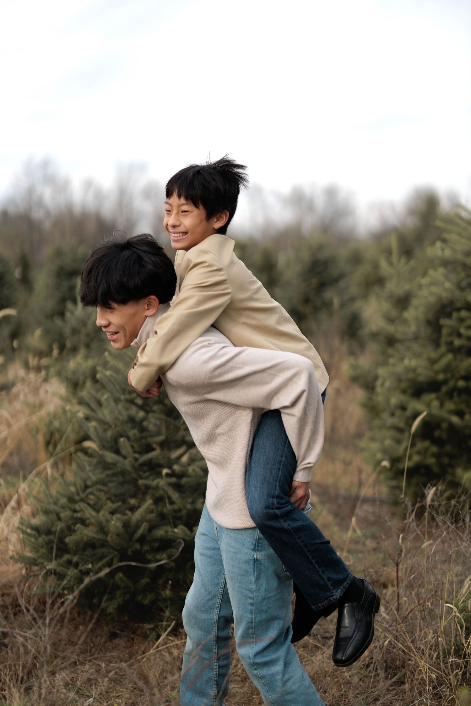 A man gives a smiling boy a piggyback ride outdoors near evergreen trees in a field.