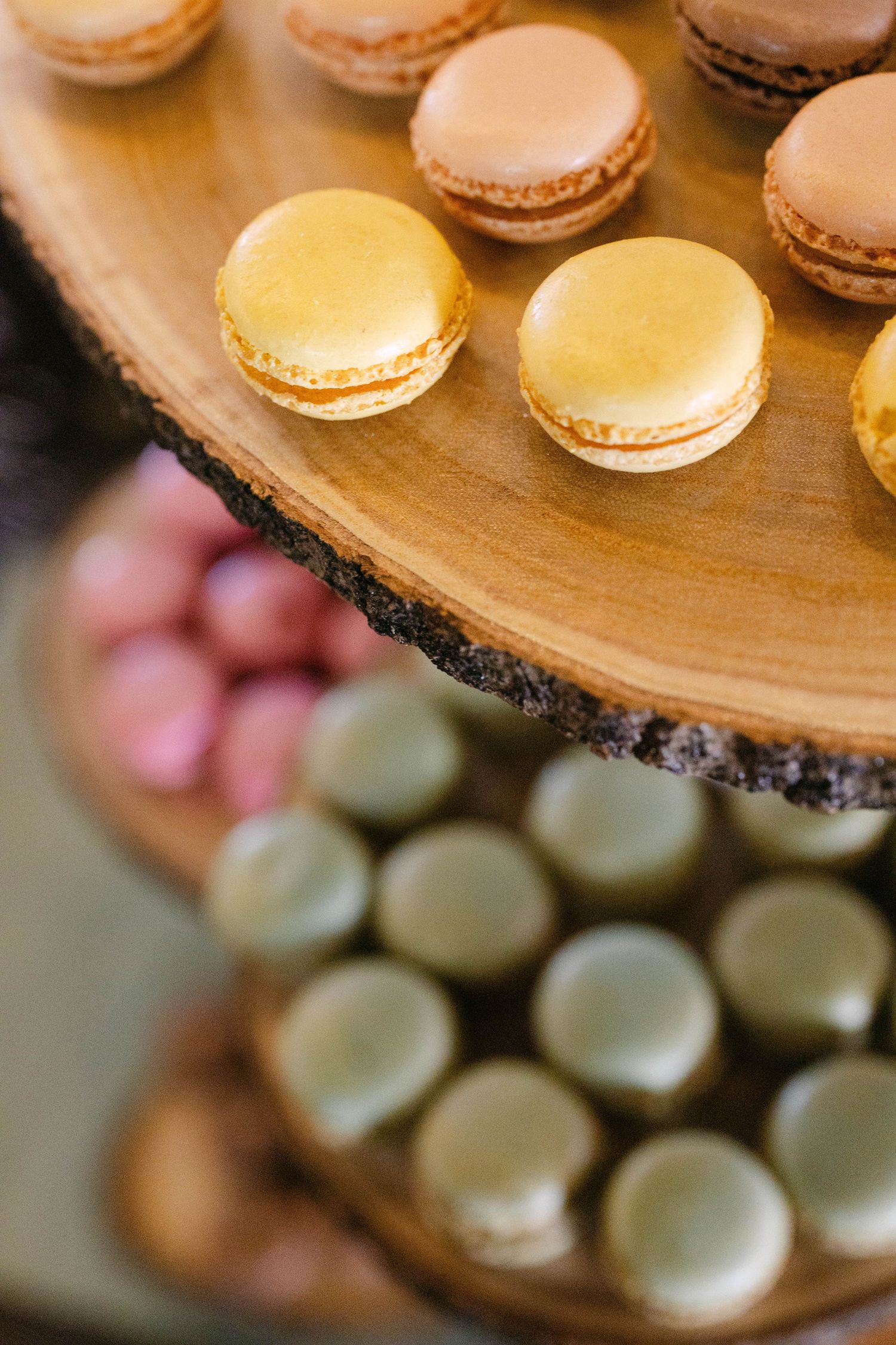 Assorted colorful French macarons displayed on rustic wooden board slices at a wedding dessert table.