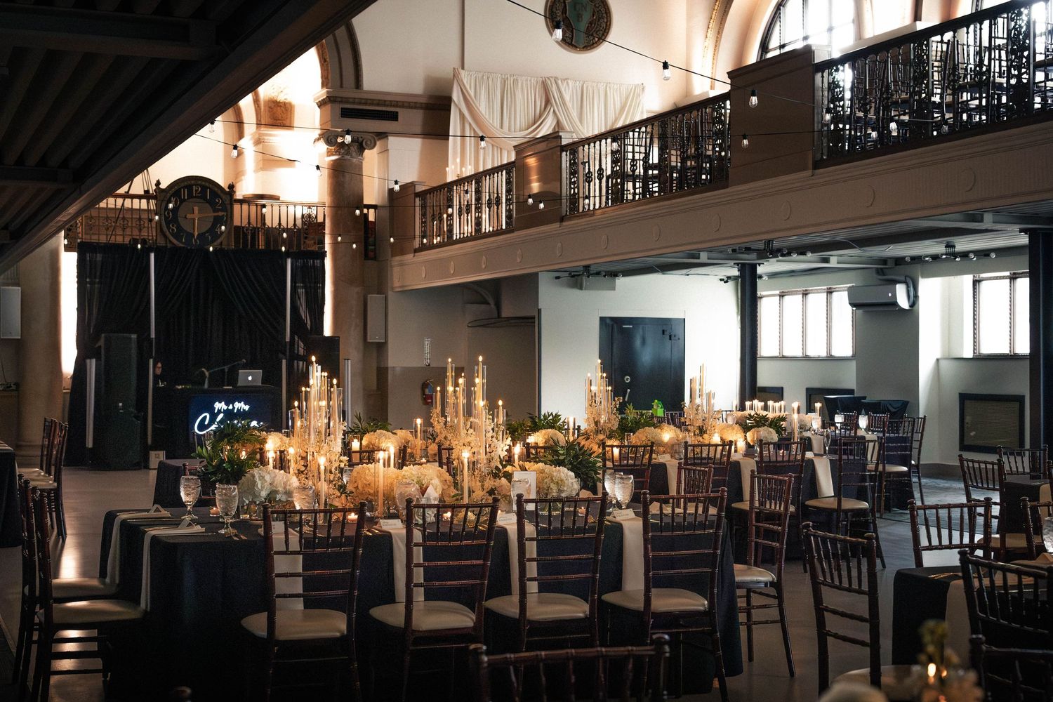 Elegant wedding reception in a historic venue with candlelit tables, chiavari chairs, and a grand mezzanine balcony.