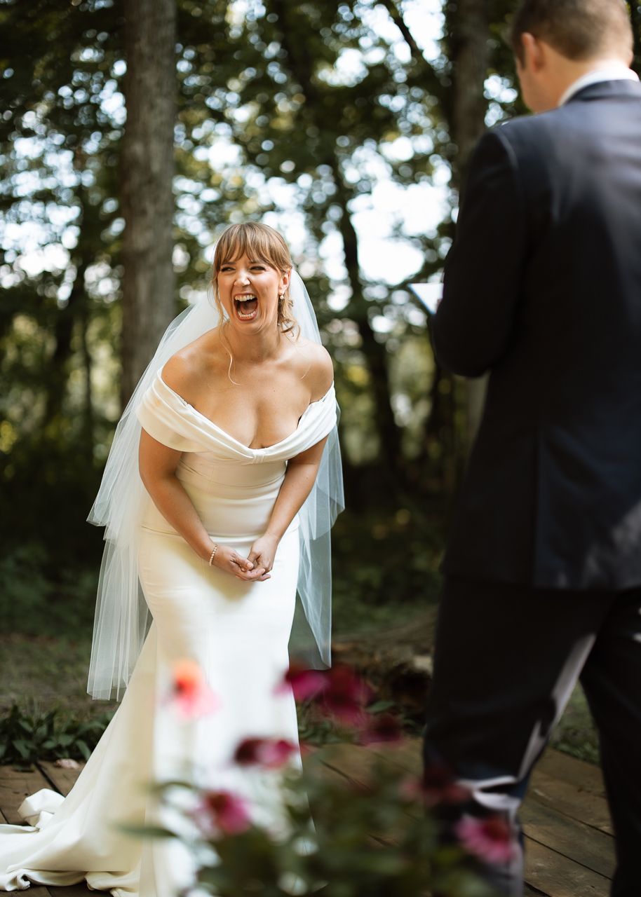 Joyful bride in an off-shoulder gown and veil laughing during an outdoor first look with her groom.