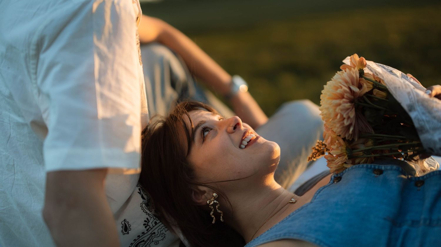 A couple in white attire shares an intimate moment during their wedding photoshoot on a beach at sunset.