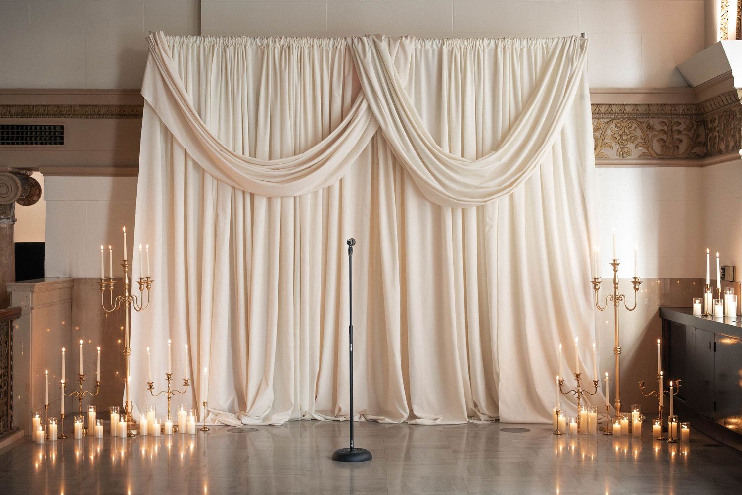 Elegant ivory draped fabric backdrop with candelabras and candles on floor for wedding ceremony.