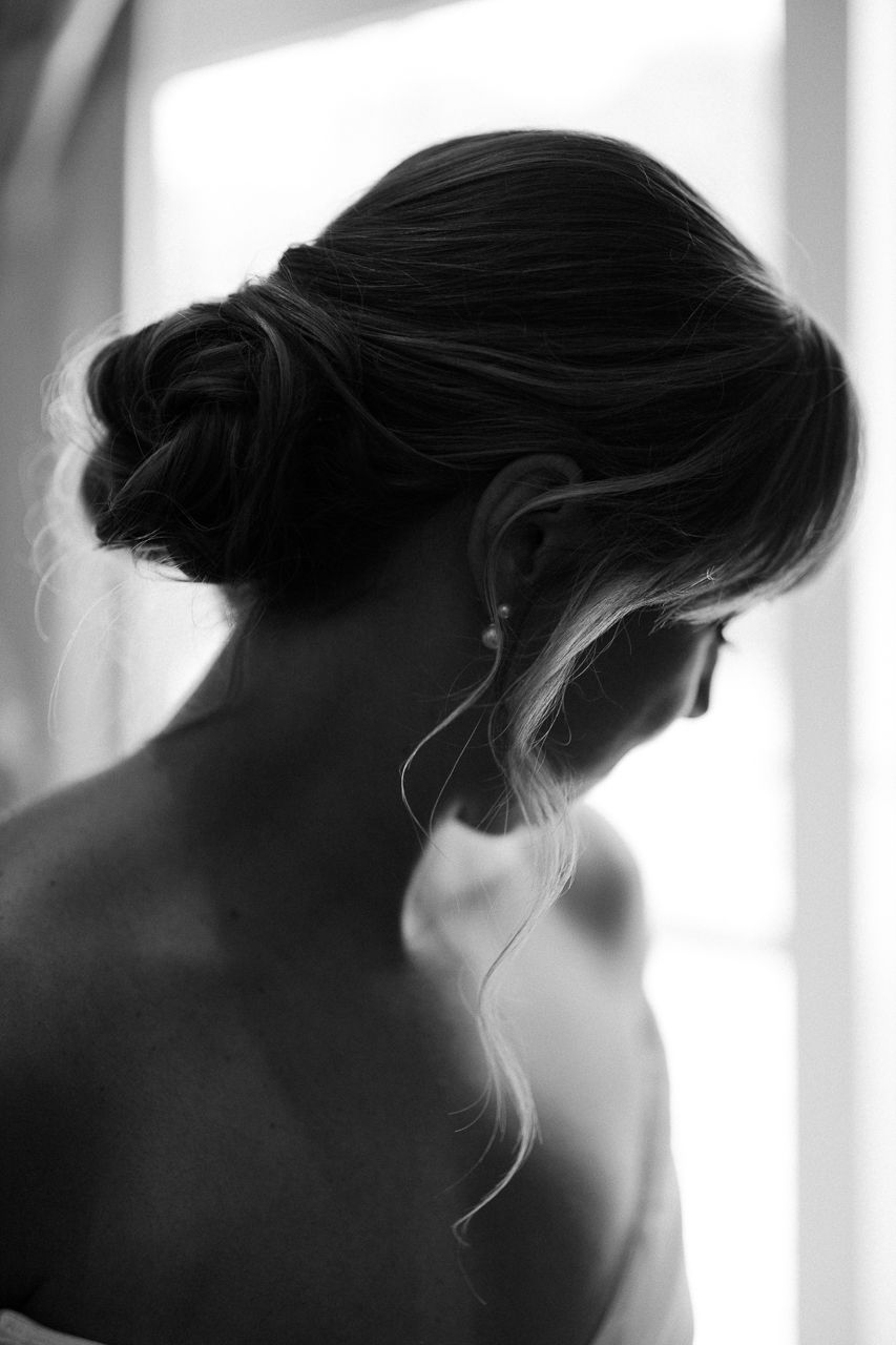 Black and white photo of a woman with an elegant updo hairstyle, loose tendrils framing her neck.